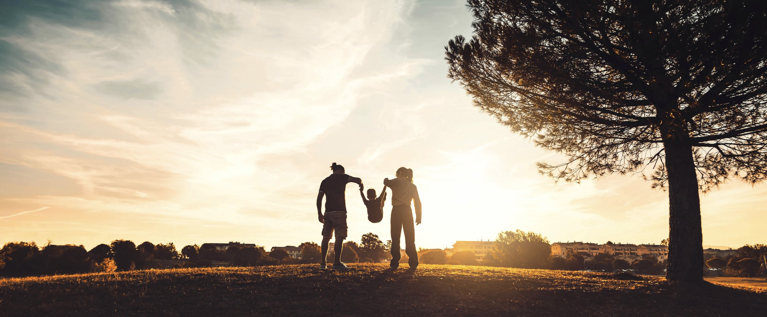 two people in a sunset swinging a child between them playing