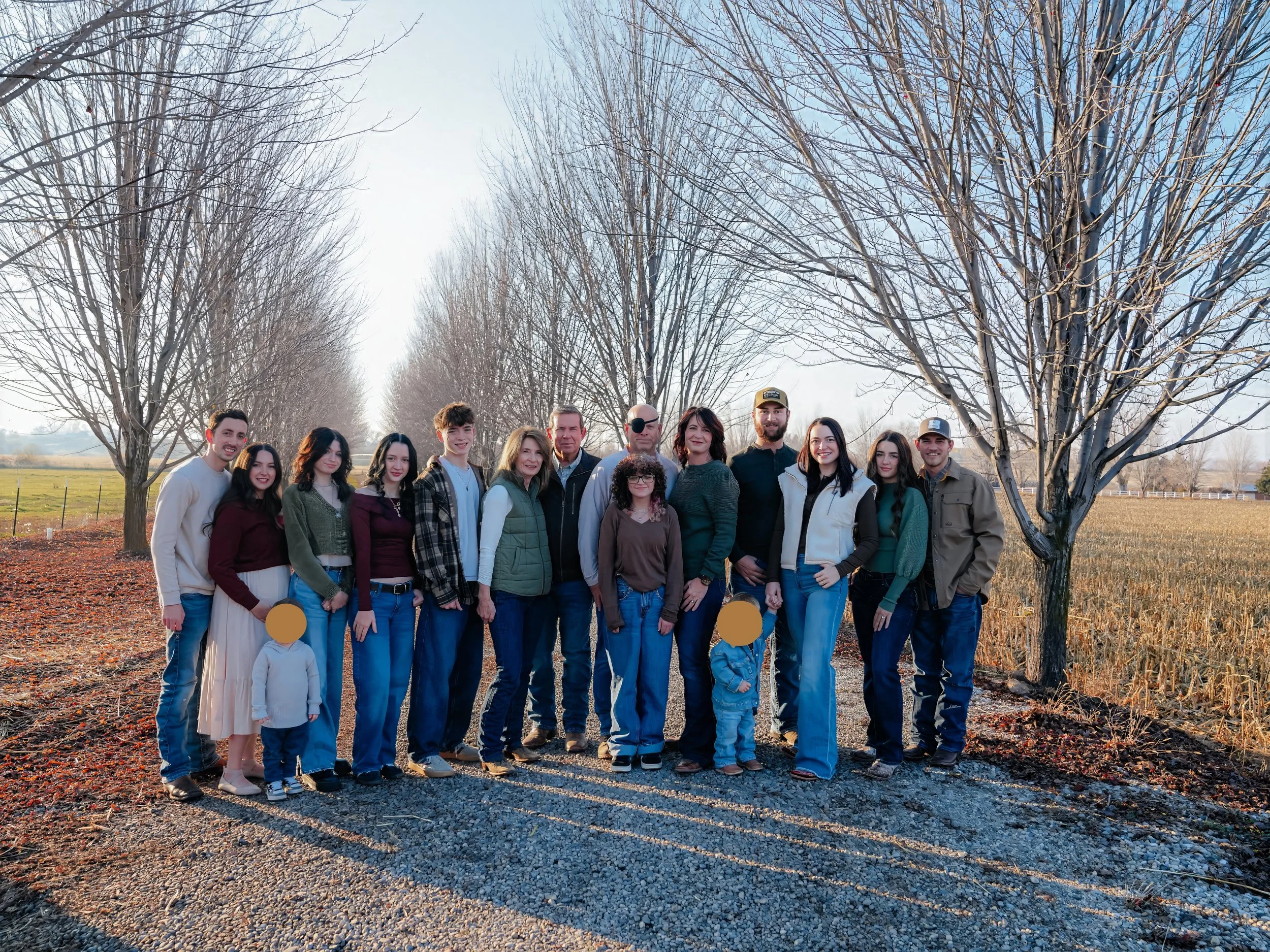 Family photo in Emmett, Idaho featuring extended family standing on colorful fall leaves with golden sunlight and autumn trees behind them.