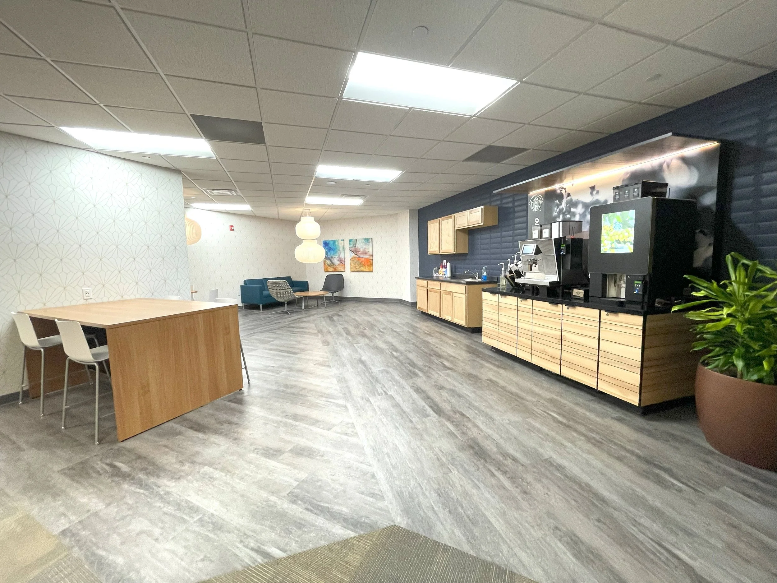 Hotel or office lounge area with a coffee station, seating area with chairs and couches, and decorative lamps and artwork