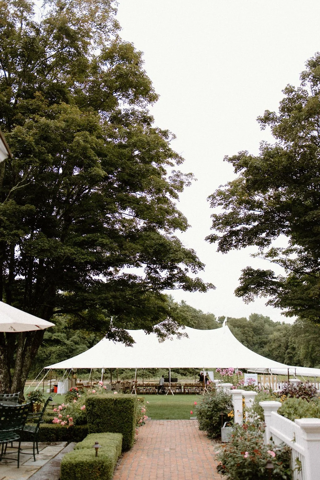 Historic estate gardens with a white wedding reception tent surrounded by mature trees.