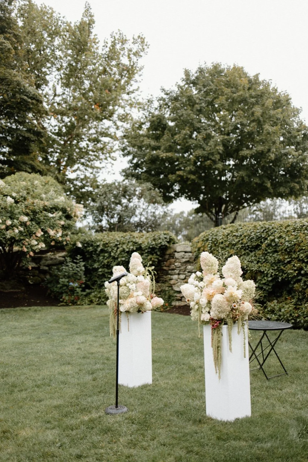 Romantic garden wedding ceremony at Smith Farm Gardens featuring a bride and groom beneath lush floral arrangements with hydrangea, spray and cottage roses, and trailing greenery in a farm estate setting.
