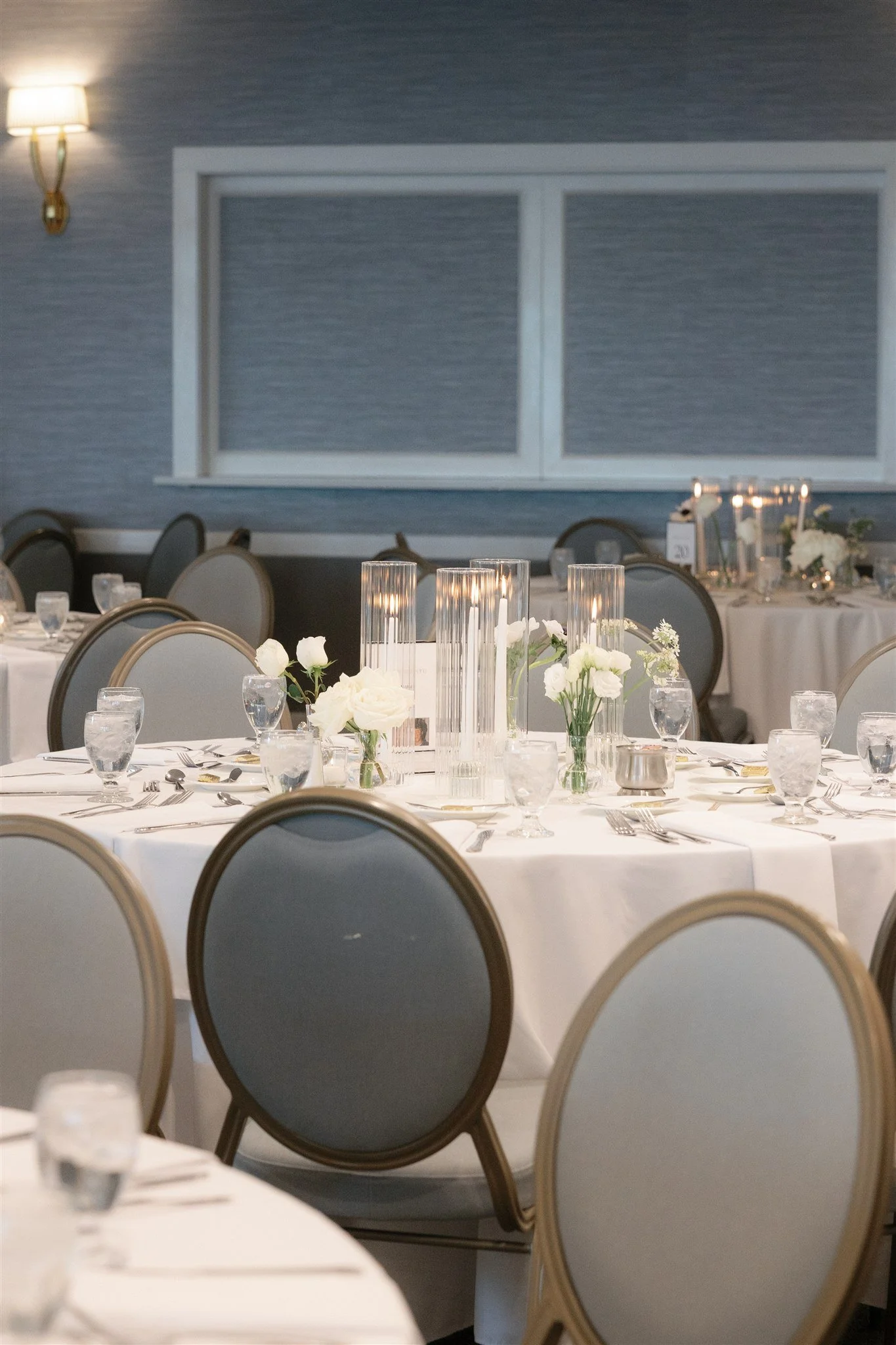 Minimal white budvase centerpieces featuring roses, lisianthus, and stock for an elegant coastal Connecticut wedding reception.