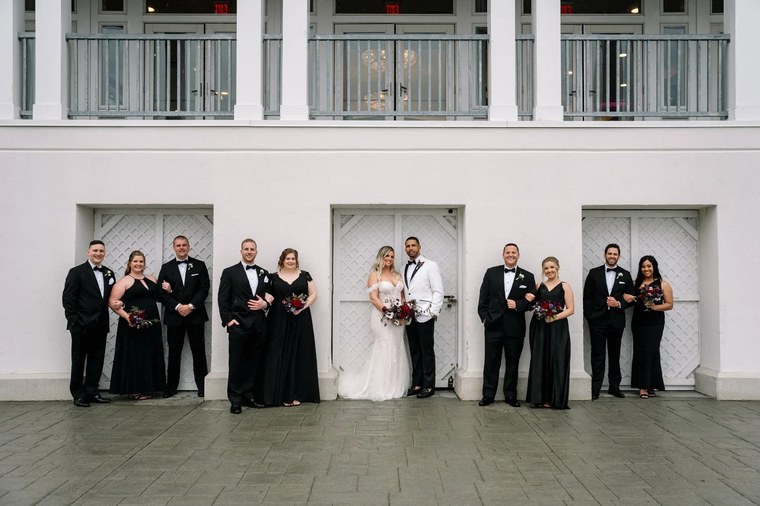Waters Edge wedding party portrait taken on cocktail patio, wedding party in black and white with bold florals by First Blush Weddings