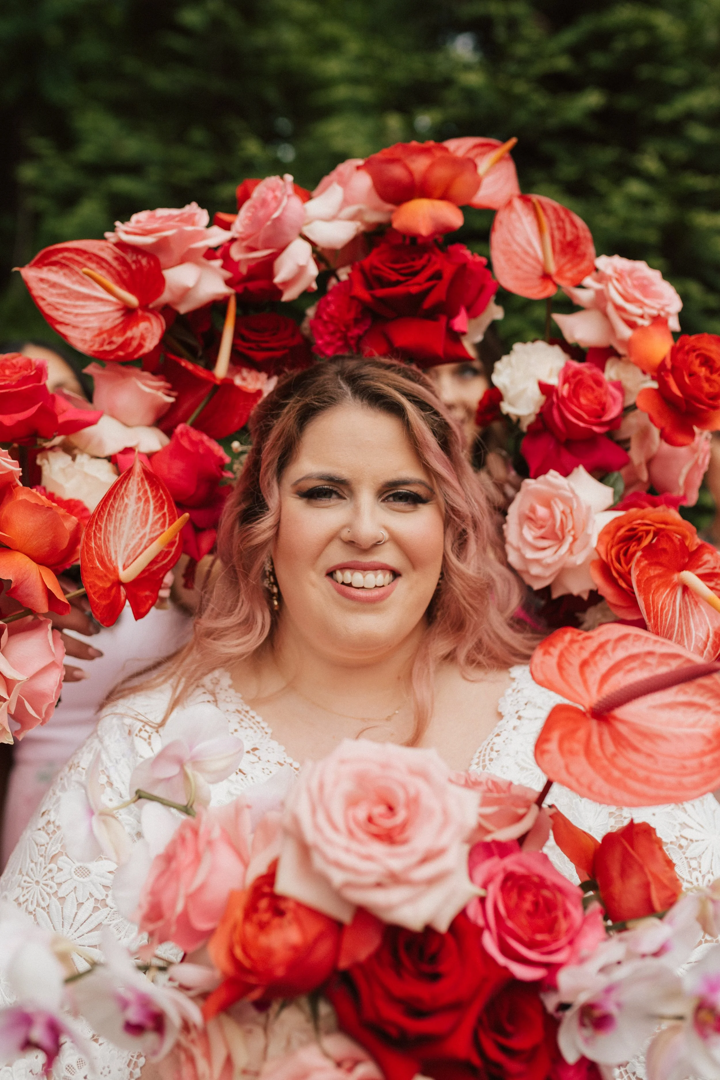 Bridal bouquet with coral, pink, and red roses, bold anthuriums, and cascading orchids in a modern garden wedding design.