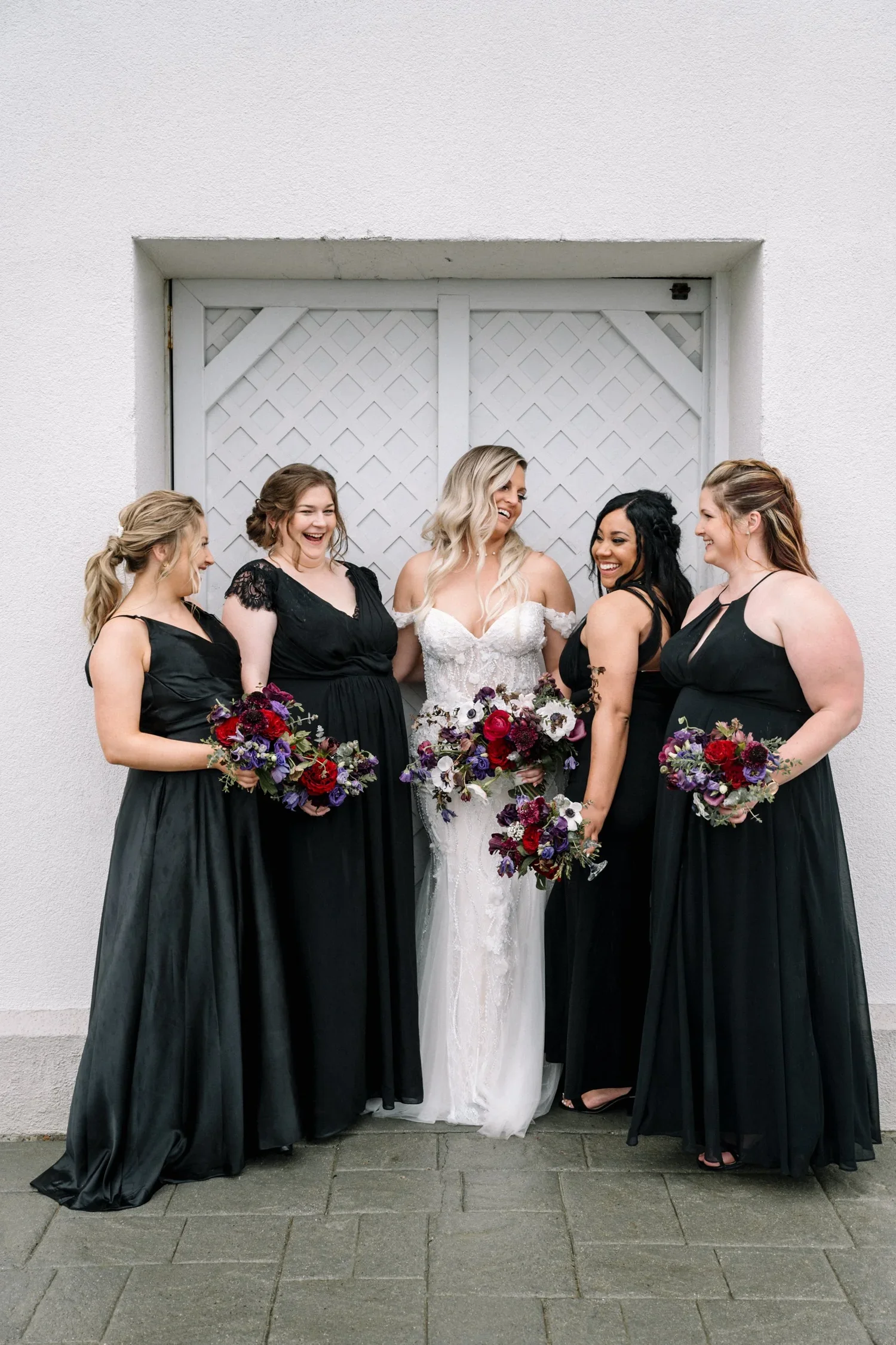 Bold jewel tone floral bouquets held by bride and bridesmaids in classic black dresses.