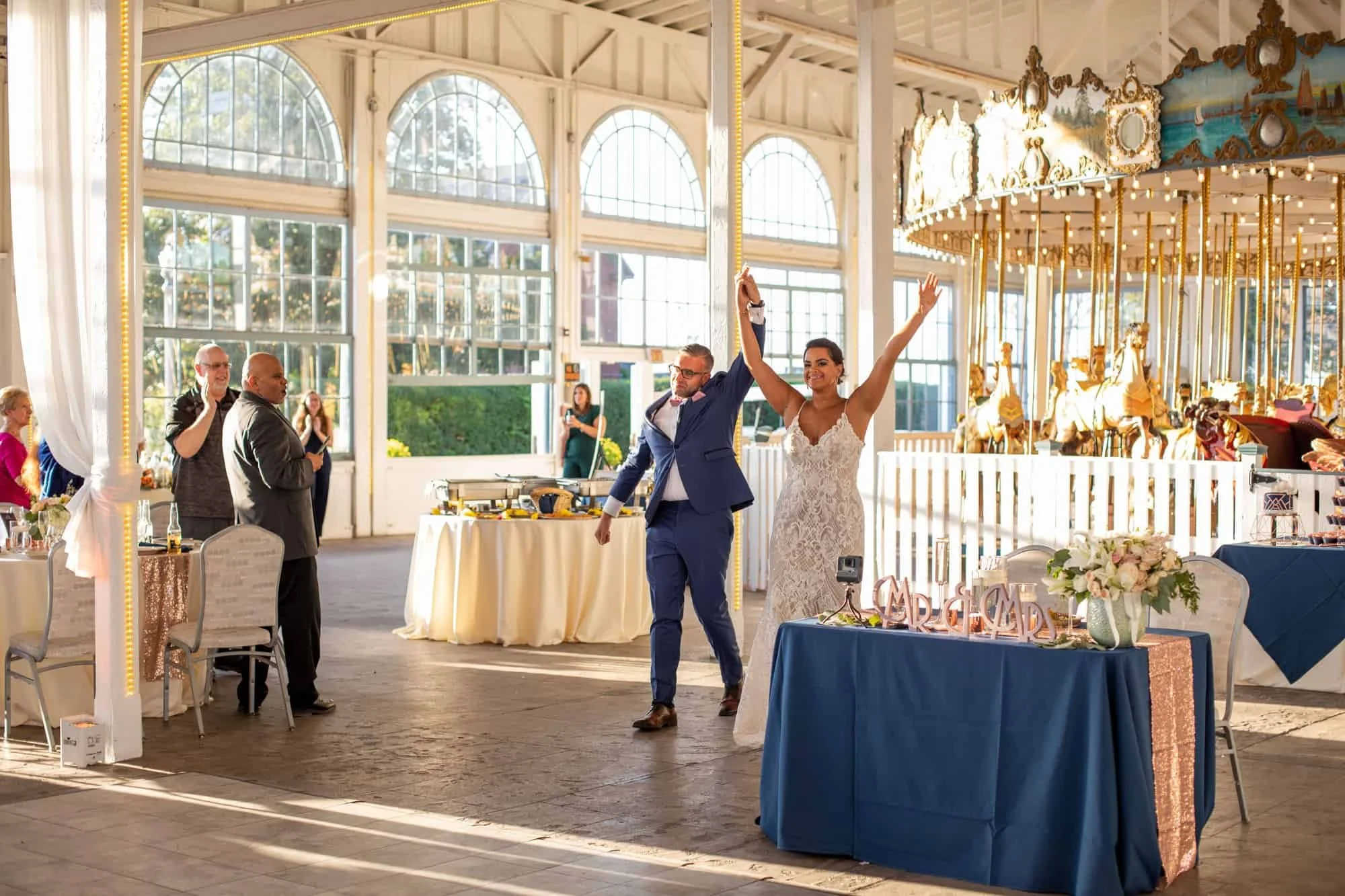 Bride and groom making a joyful grand entrance beside the antique carousel at a Lighthouse Point Park wedding reception in New Haven