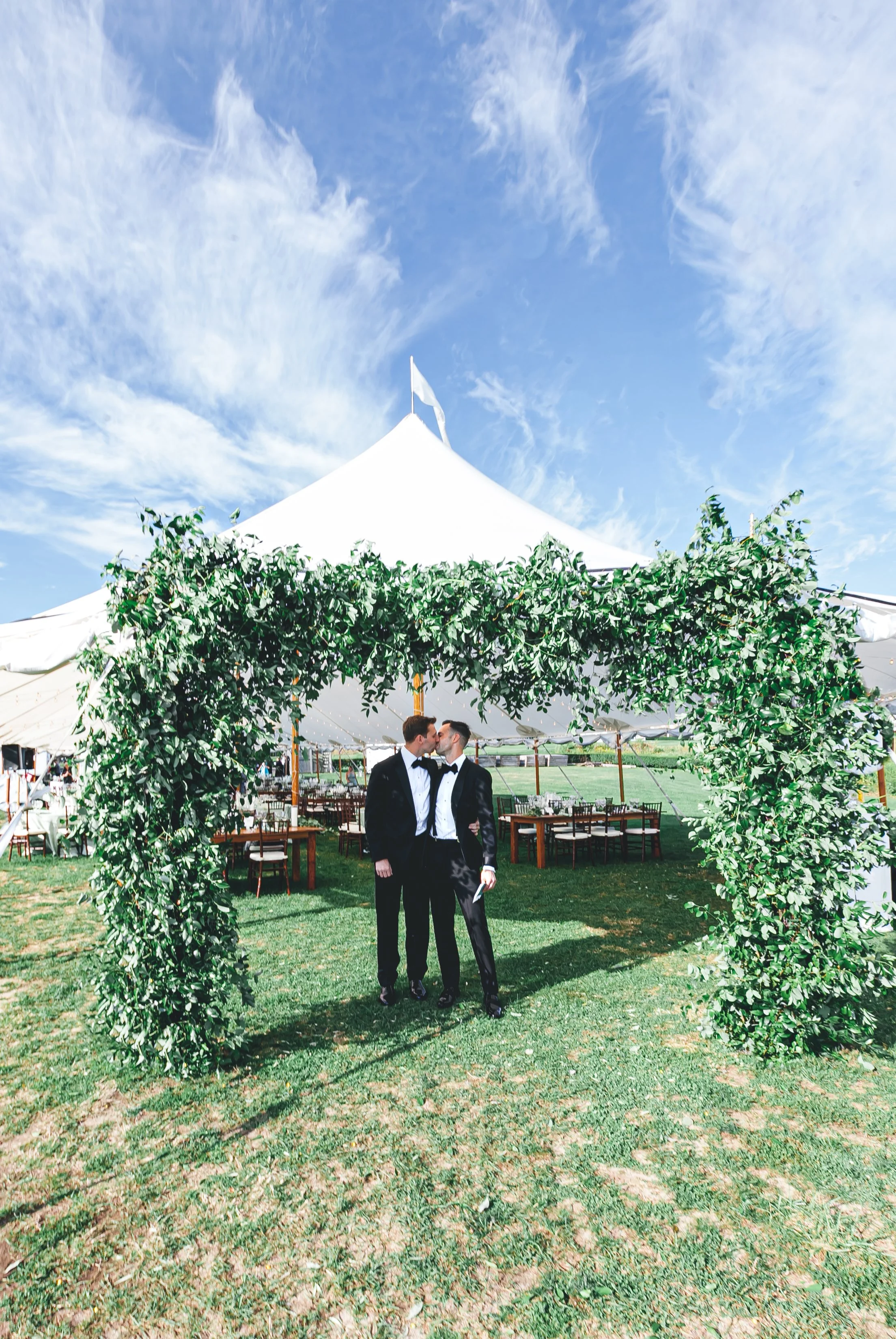 A sailcloth tent with white flags rises behind a greenery-wrapped entrance arch at a private Saybrook Point wedding reception