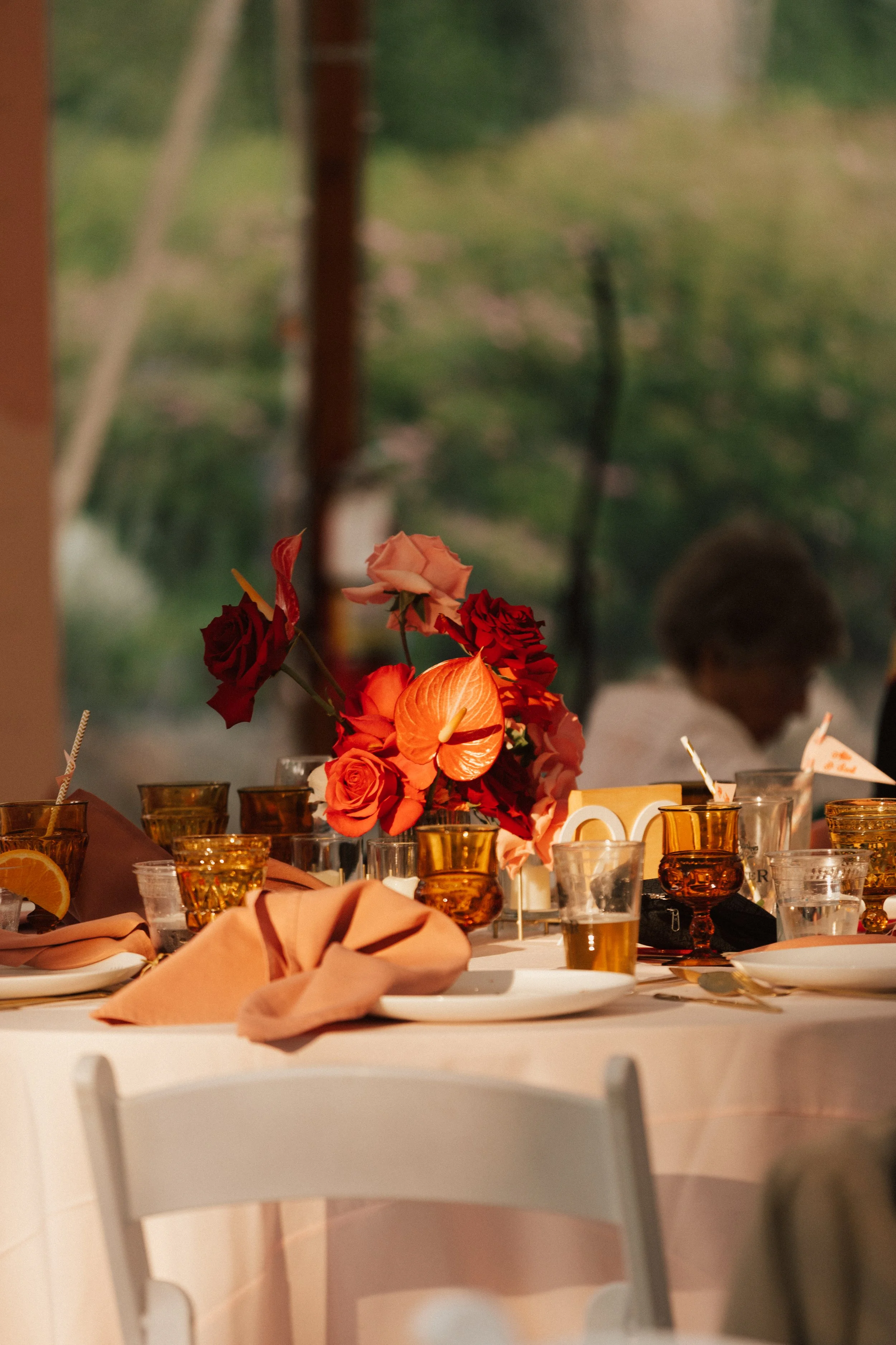 Modern floral centerpiece with pink and coral roses, set beside sleek amber glassware and gold accents.