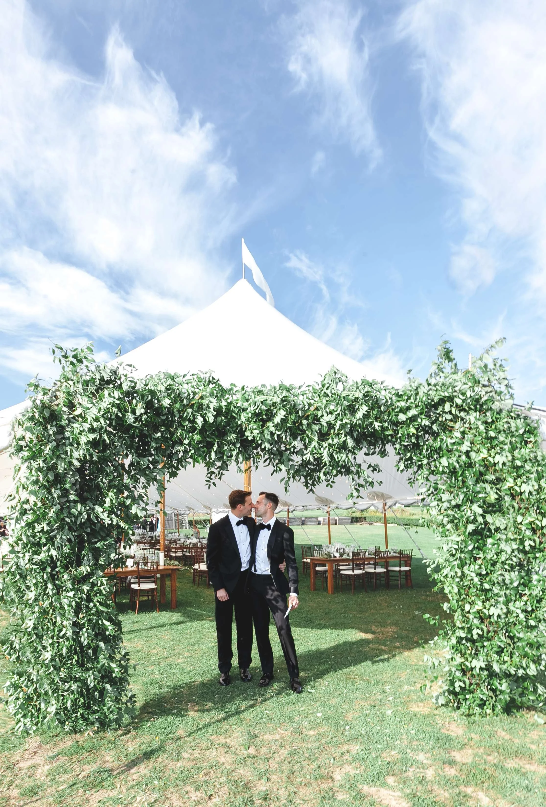 two grooms under east coast wedding tent entrance covered in greenery