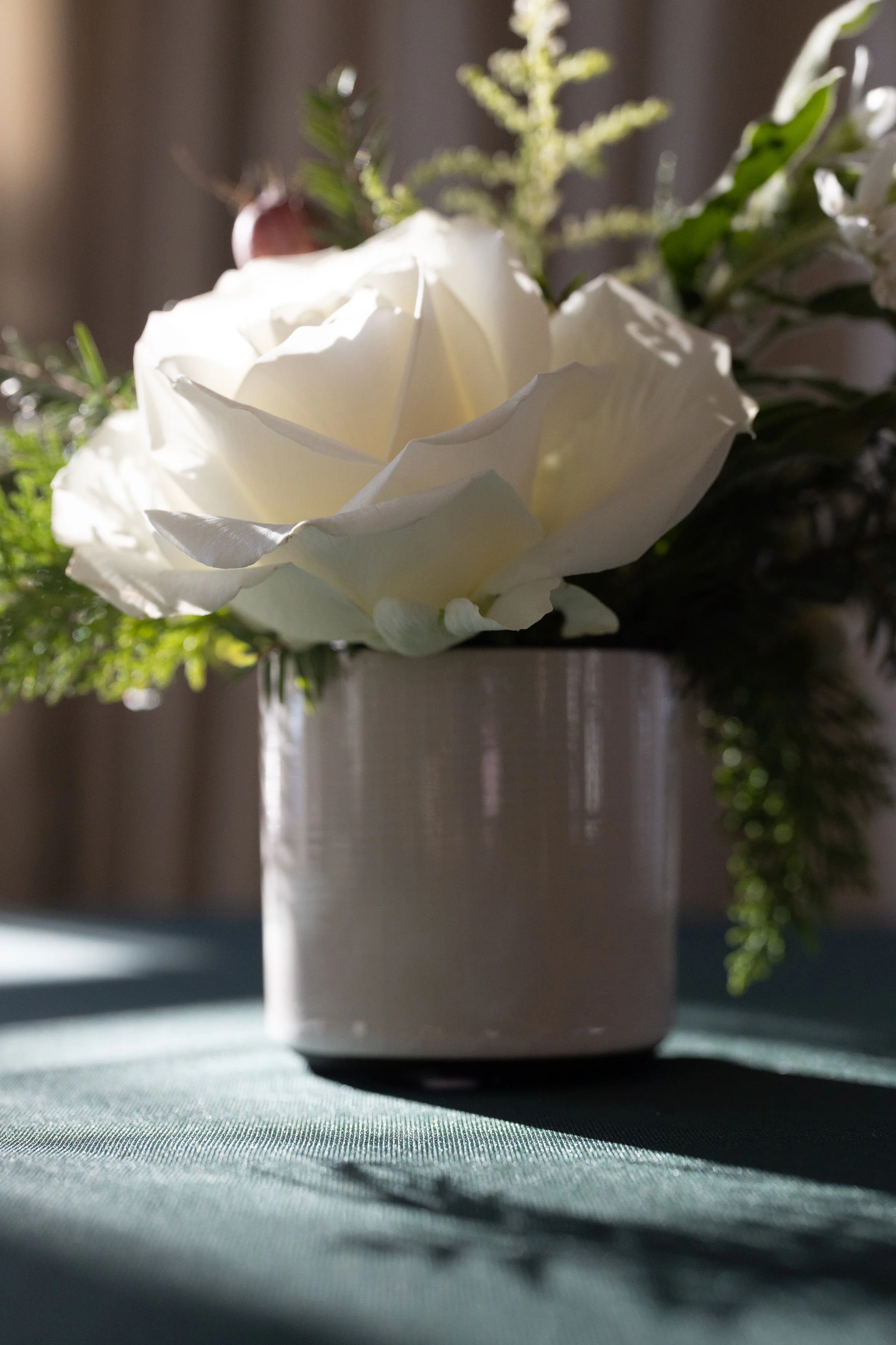 Overhead view of a small winter arrangement with spruce, pine and white blooms in a white ceramic pot beside a glowing votive