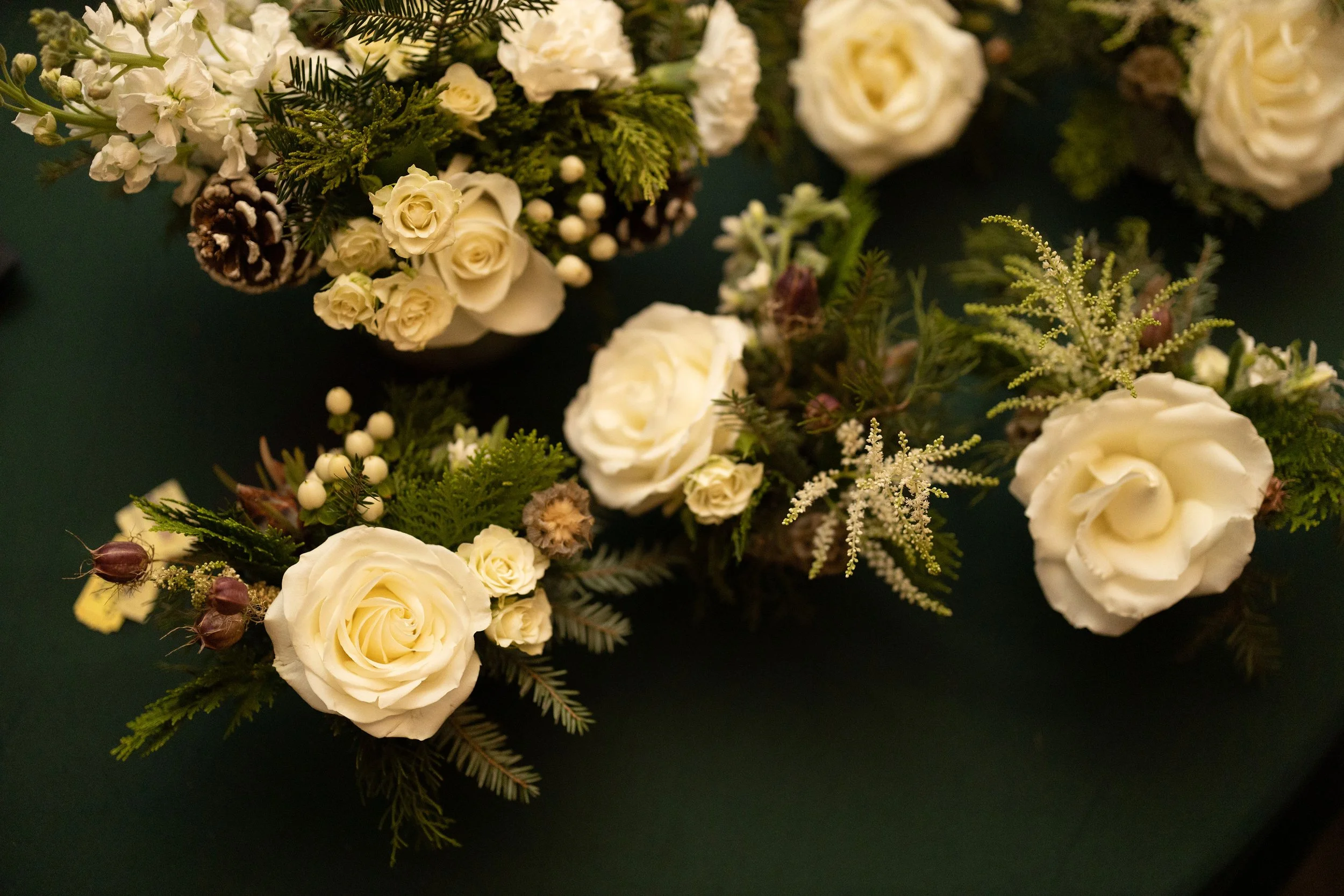 Side view of a low winter centerpiece with white roses, astilbe and evergreen foliage in a white ceramic pot
