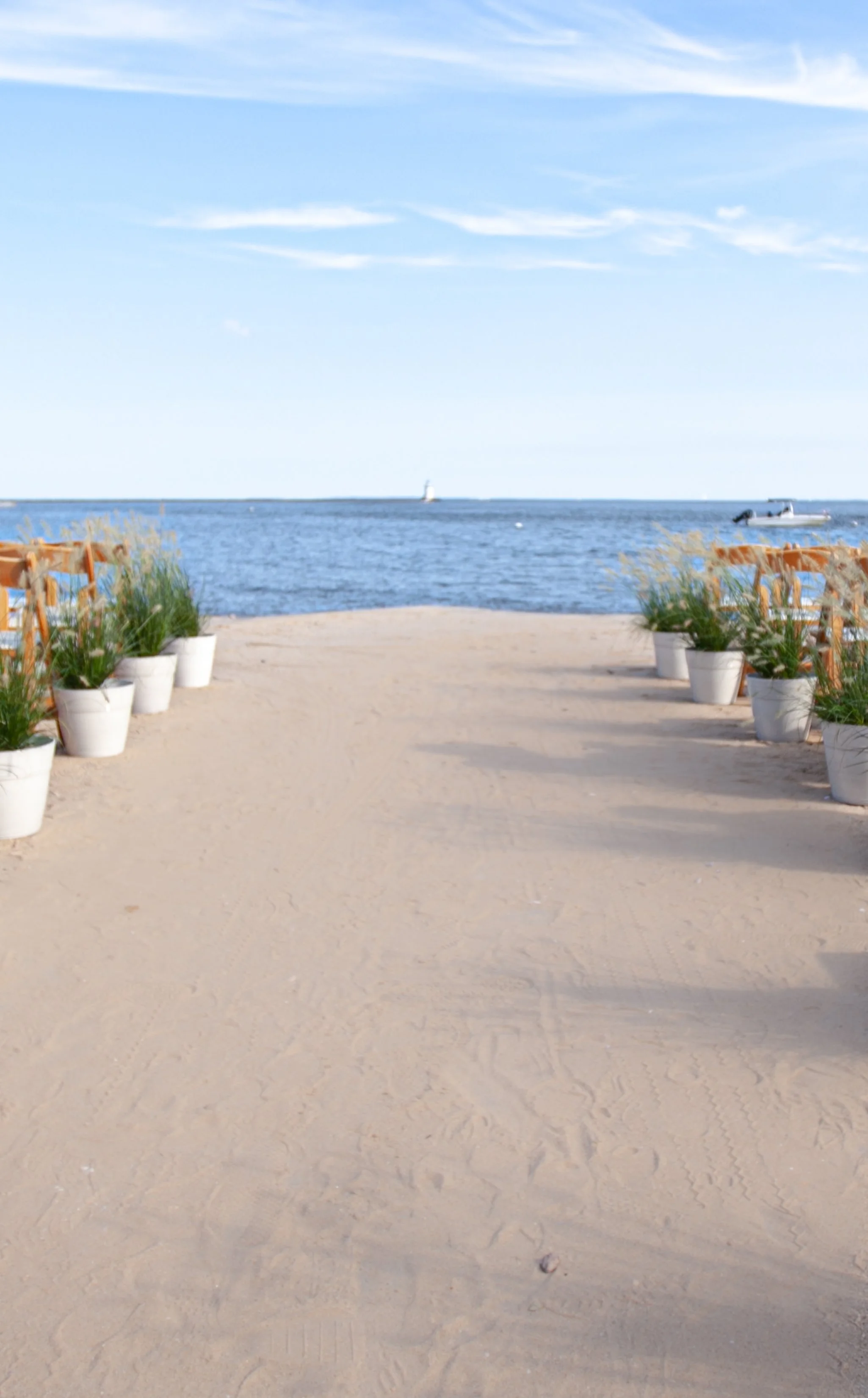 Potted ornamental grasses line a sandy ceremony aisle, softening the rows of wooden folding chairs at Saybrook Point.