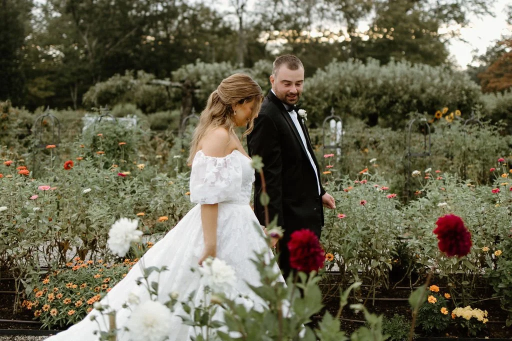 Bride and groom walk through a late-summer flower garden at Smith Farm Gardens during their romantic Connecticut wedding.