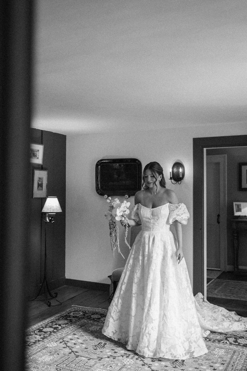 Black and white bridal portrait of Gaby wearing a romantic off-the-shoulder floral wedding gown and holding an airy white bouquet with trailing amaranthus.
