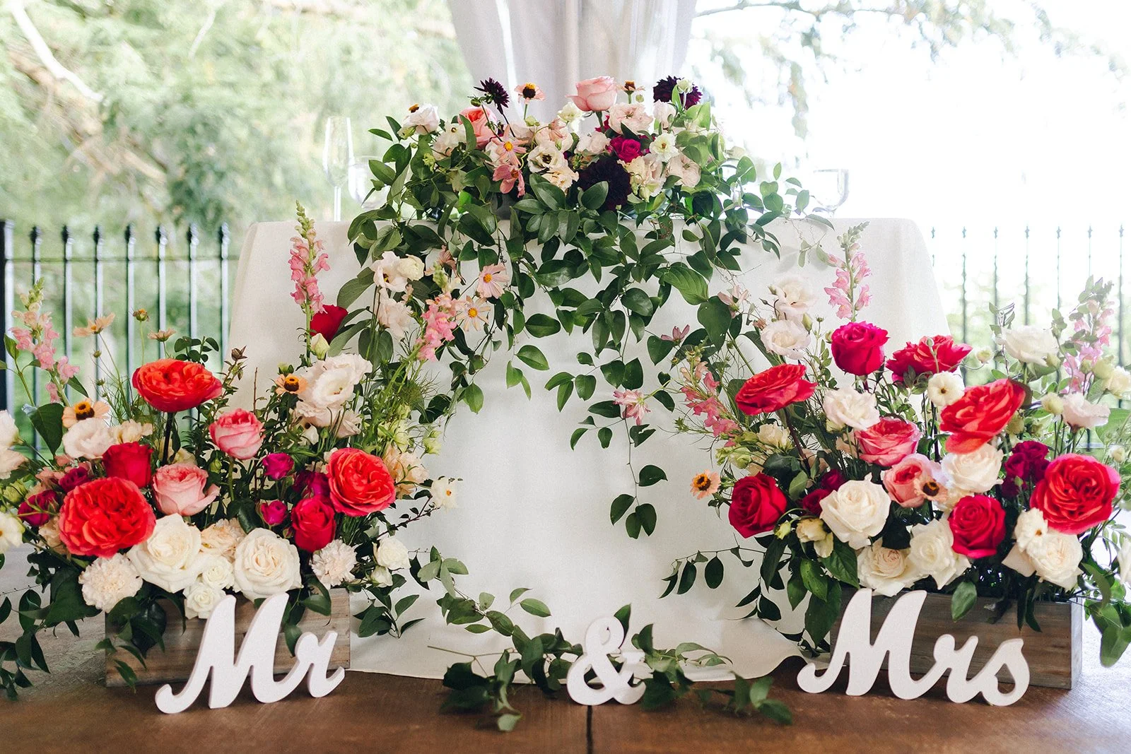 Romantic sweetheart table decorated with abundant pink, coral and white wedding flowers, trailing greenery and Mr and Mrs signs at Wickham Park.