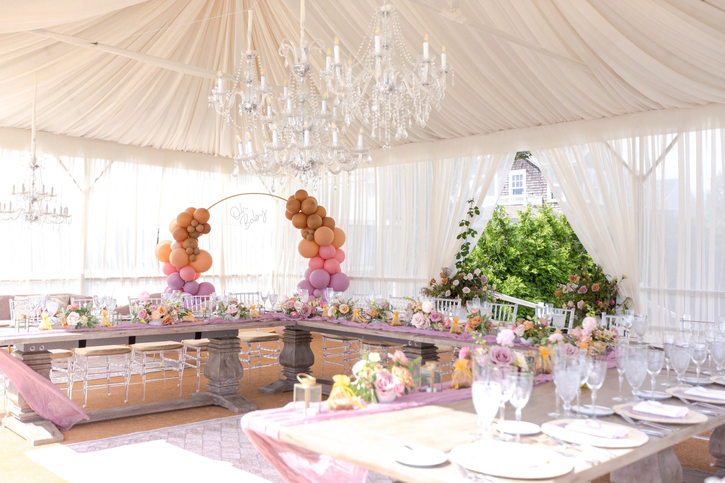 Interior of a draped tent baby shower with chandeliers and long tables