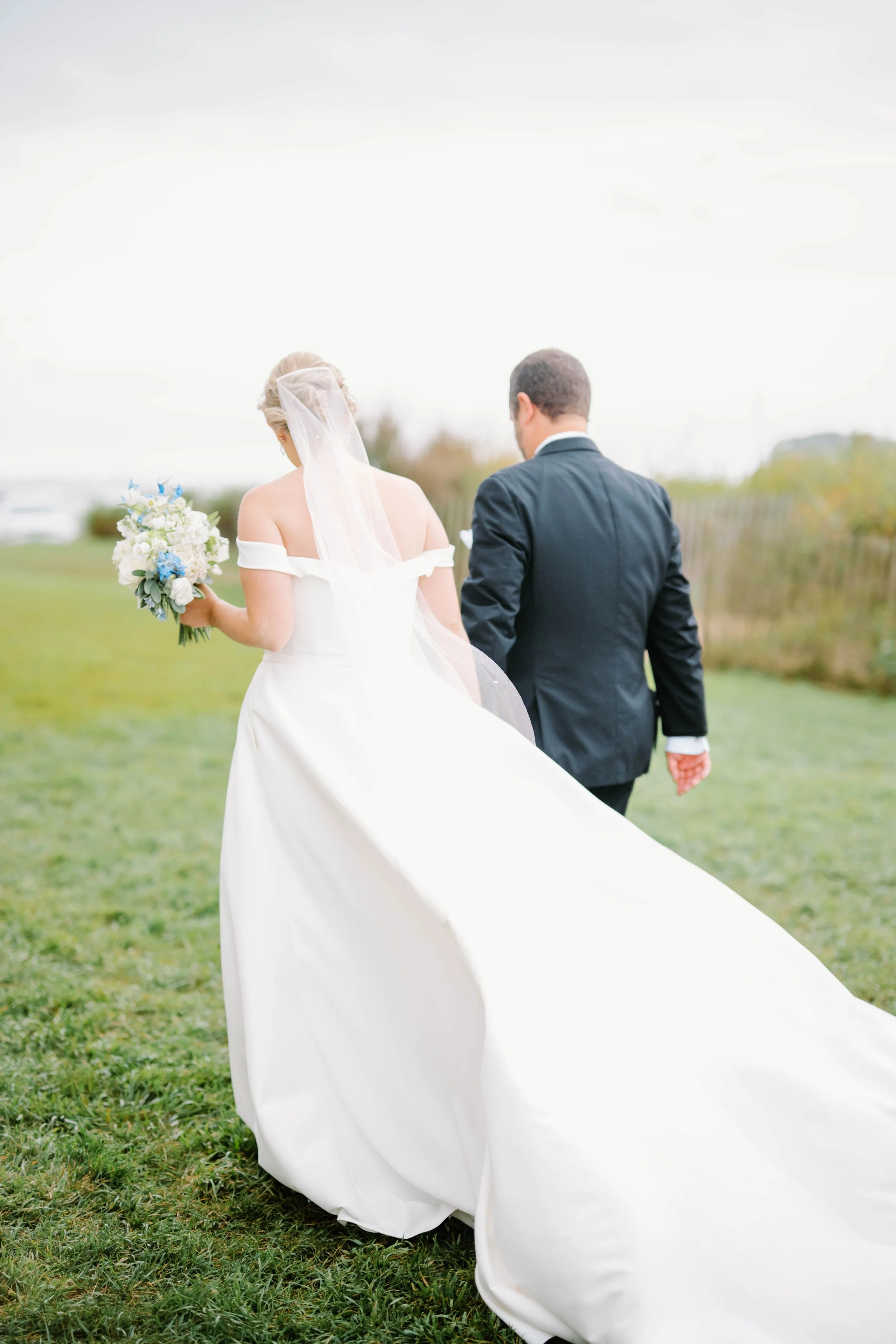 Bride and groom portraits on beach; groom in black tux, bride holding blue and white bouquet.