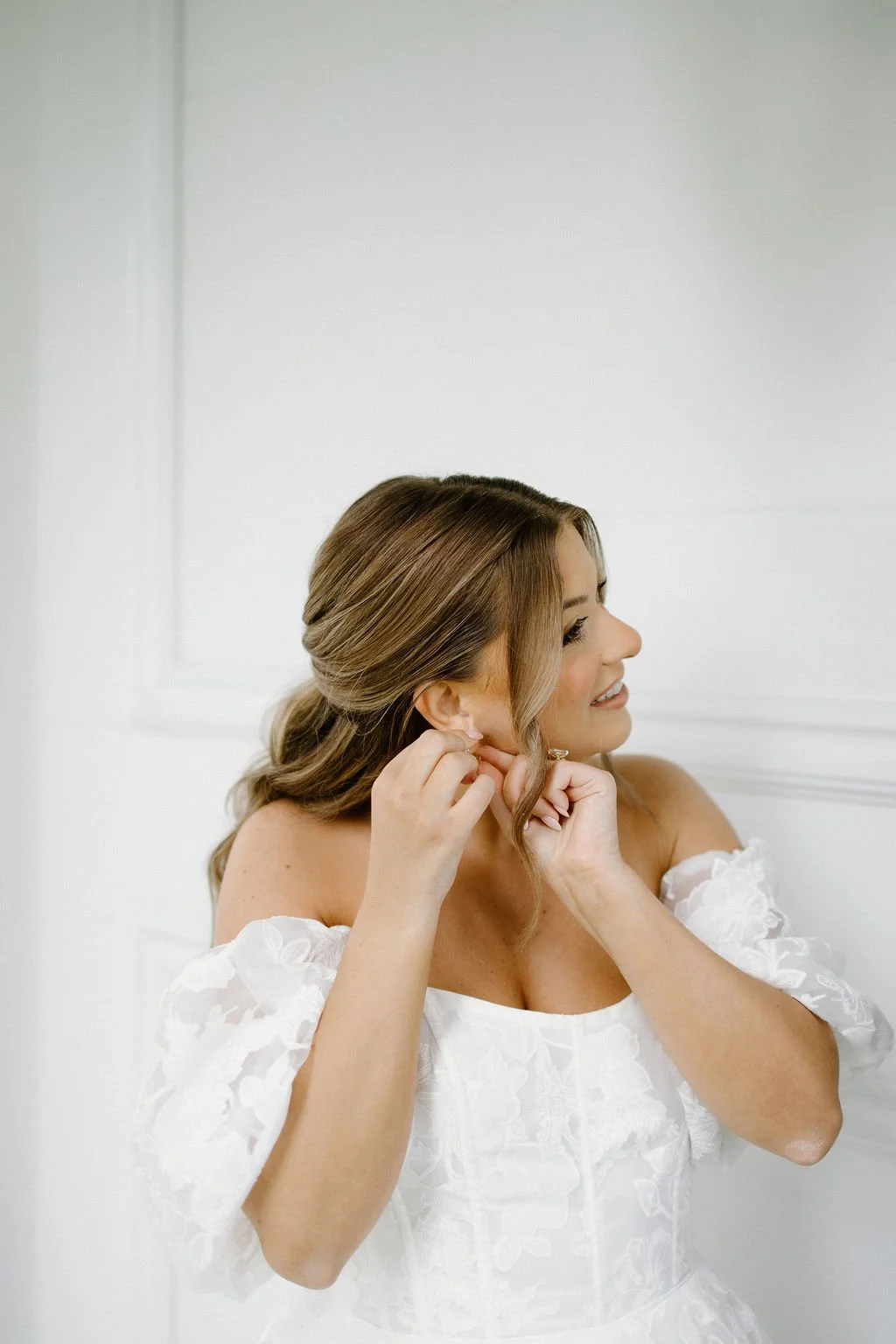 Bride wearing an off-the-shoulder white wedding gown and delicate earrings.