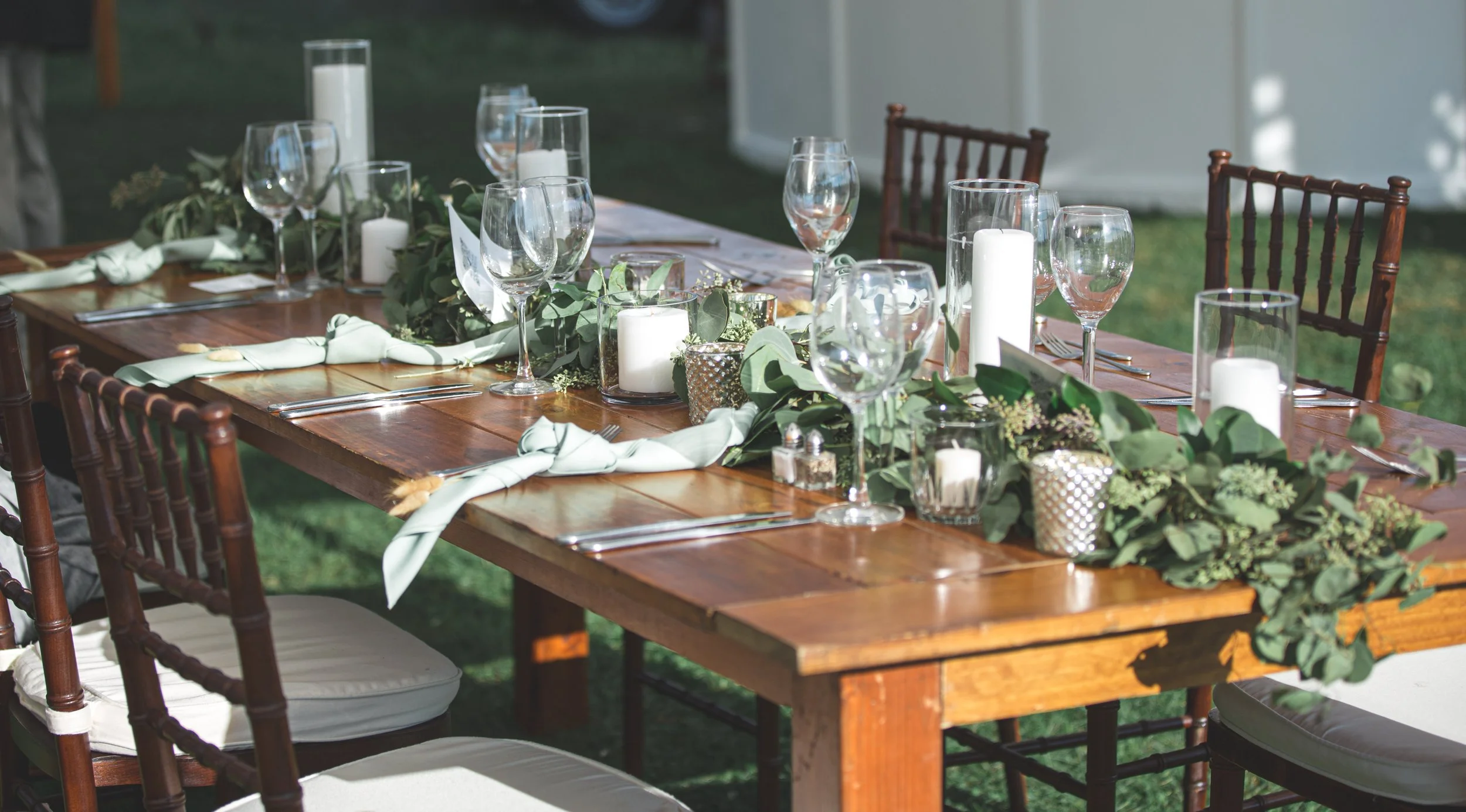 A trailing eucalyptus garland winds down a sage-linen table, punctuated by clusters of pillar candles at a Saybrook Point reception.