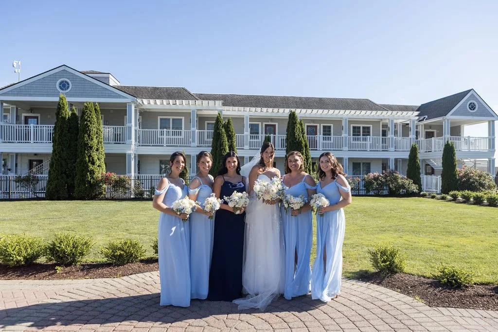 Full bridal party portrait at Water's Edge Resort and Spa Connecticut featuring mix of light blue and navy bridesmaid dresses with white and blue bouquets by First Blush Floral Design