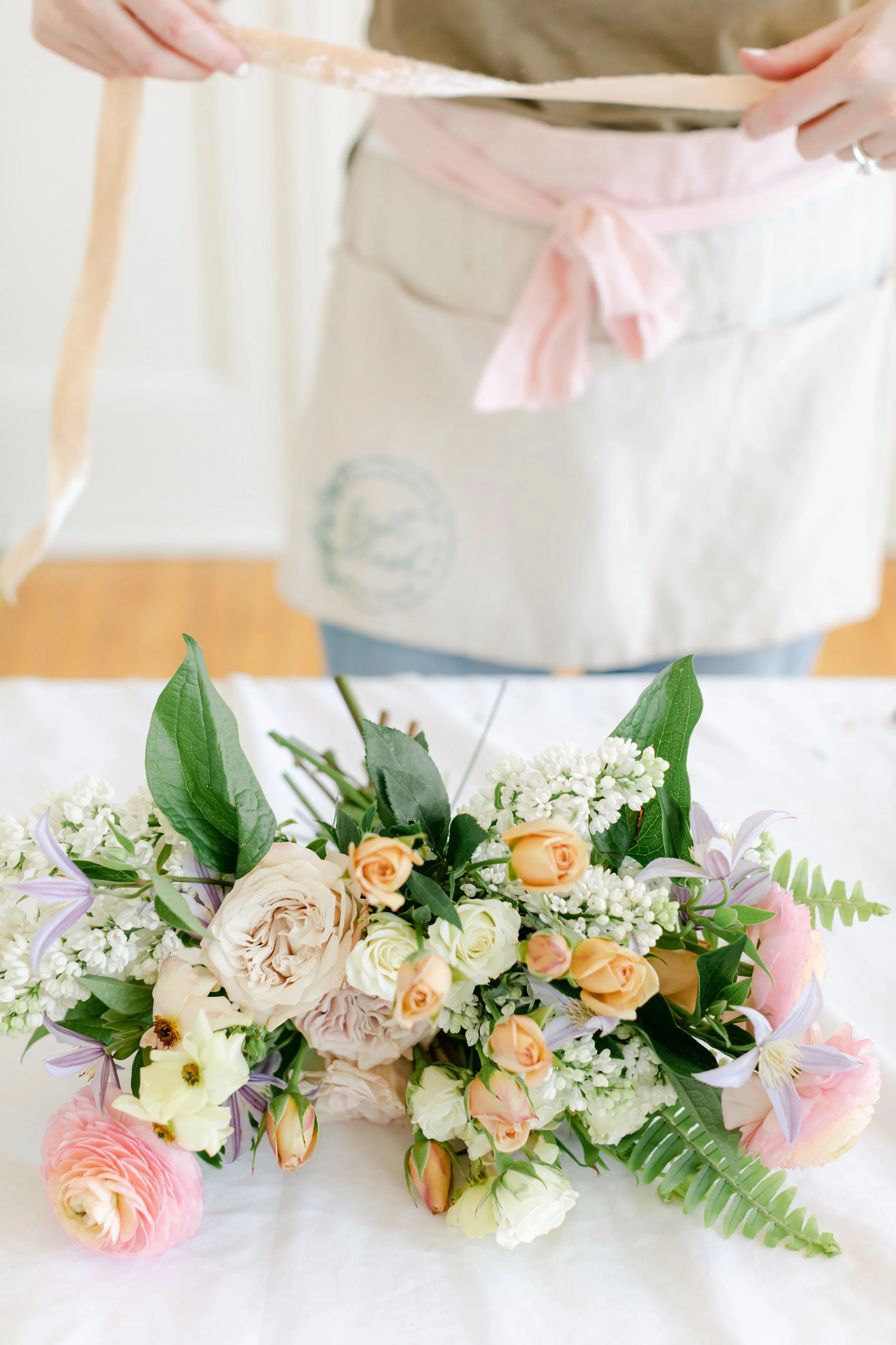 Floral designer and event planner emma machugh from first blush weddings uses a handmade silk-dyed ribbon to tie a bridal bouquet.
