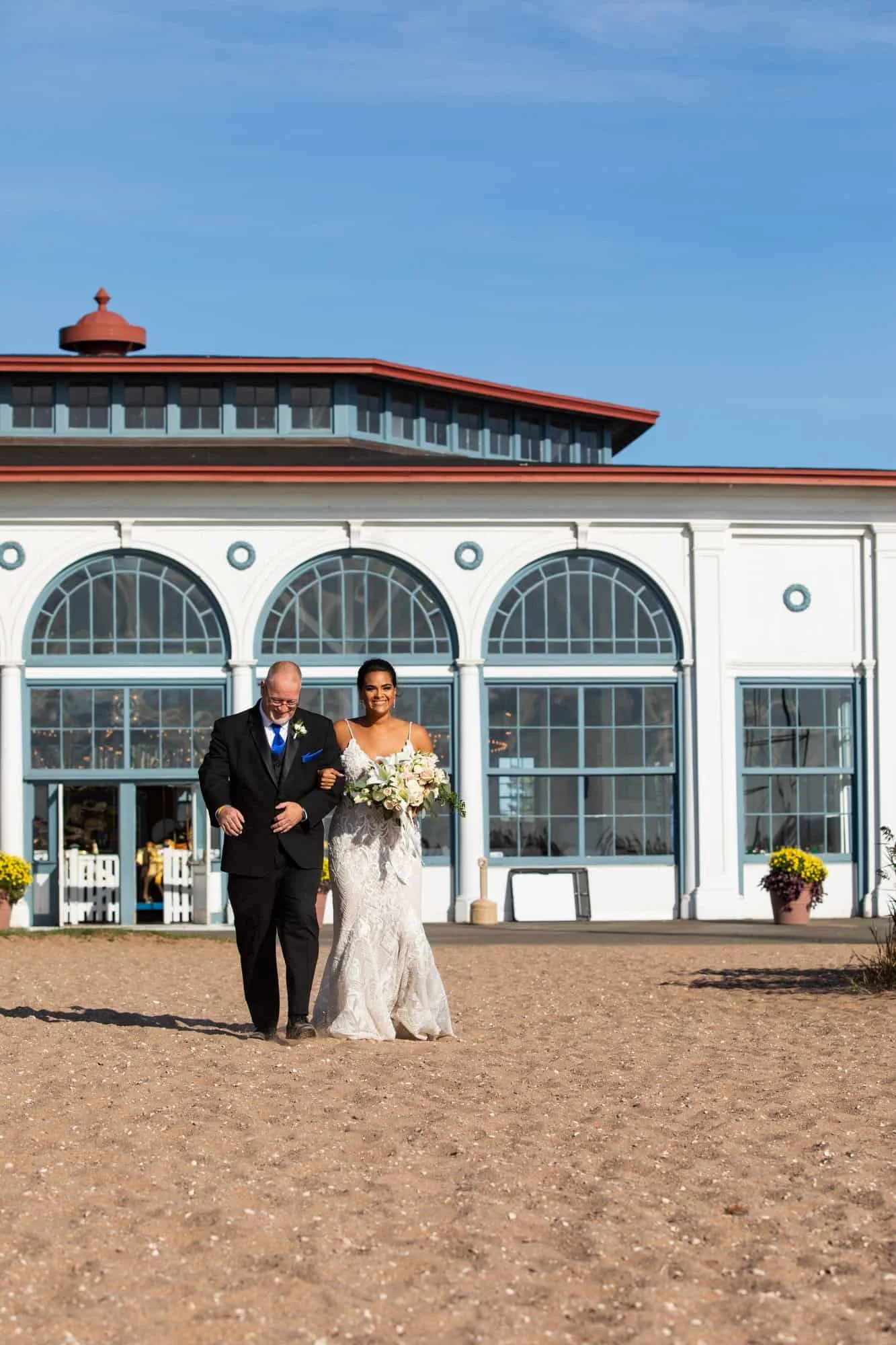 Beach wedding ceremony on the sand at Lighthouse Point Park in New Haven, Connecticut, with the bride holding a white lily bouquet