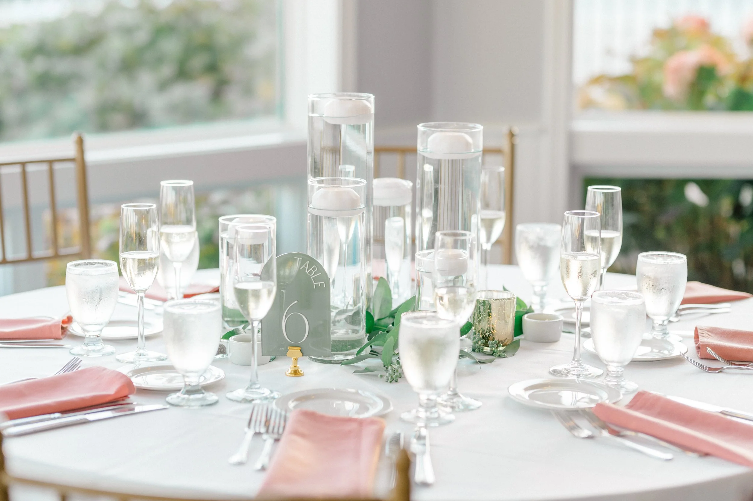 Modern candle centerpiece with loose greenery for seaside reception.