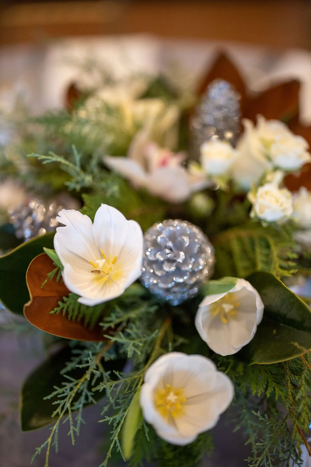 Winter arrangement of magnolia leaves, cedar, white roses, spray roses, white tulips and an orchid in soft window light