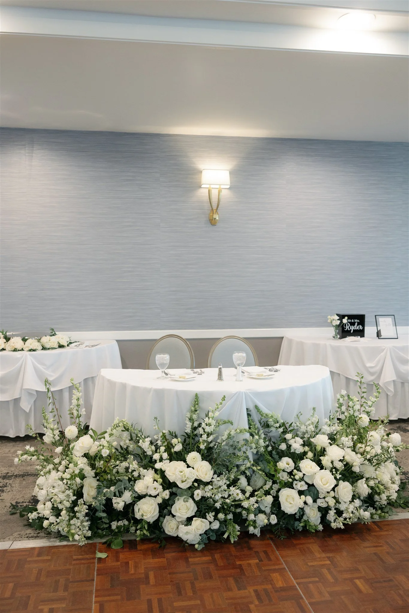 An all-white ceremony flowers set in front of the sweetheart table. 
