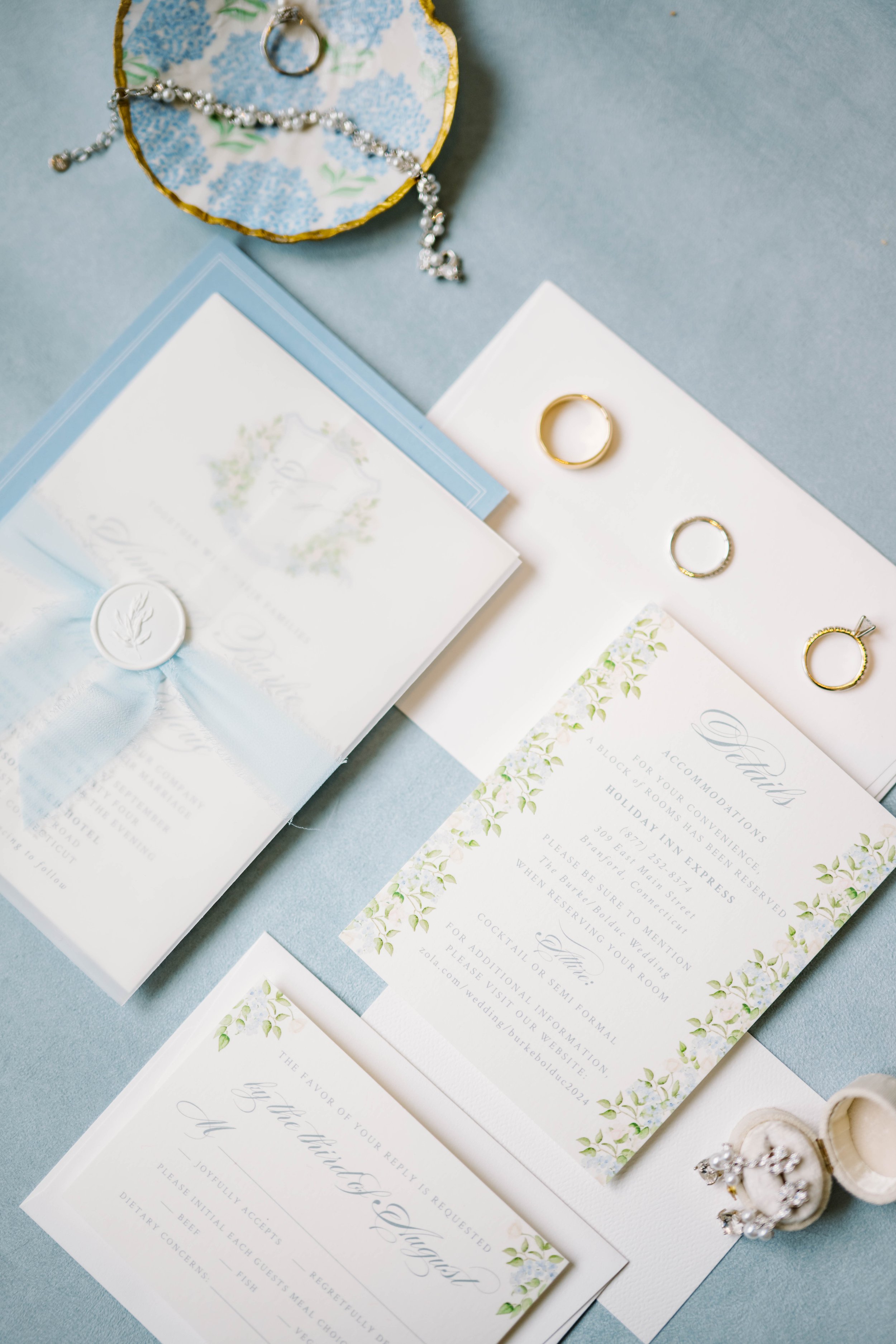 Flat lay of coastal blue wedding invitation suite by Rebecca Green Design with floral accents.