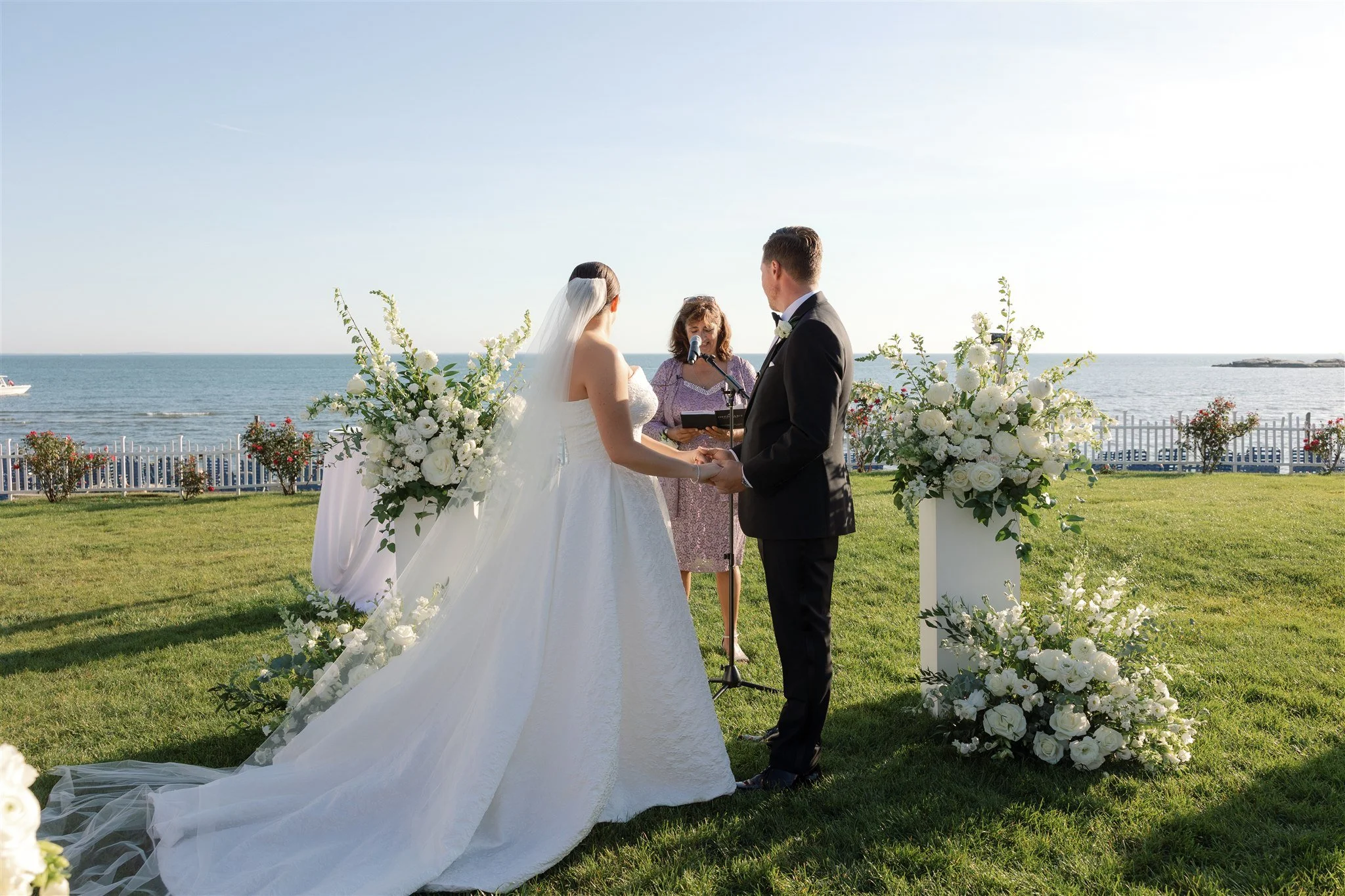 Grounded white floral meadows anchoring the ceremony columns on the Water’s Edge lawn.
