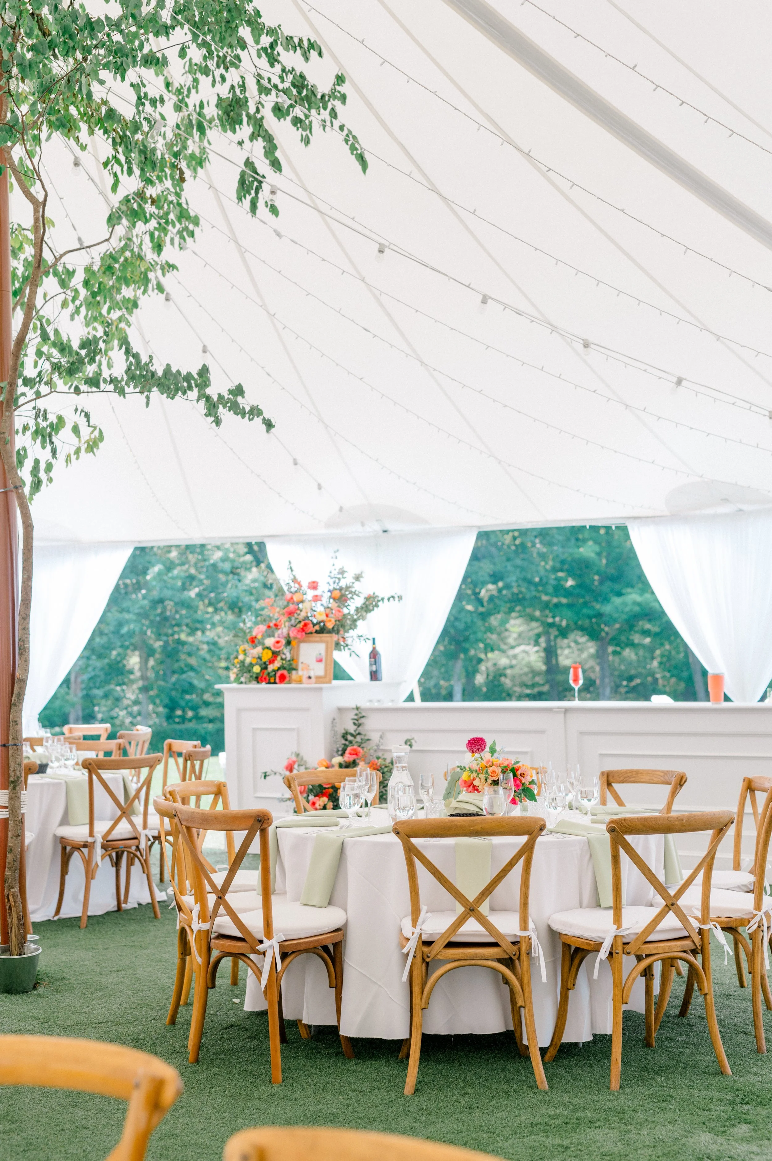 Low compote centerpieces in coral, peach, and golden yellow under sailcloth tent.