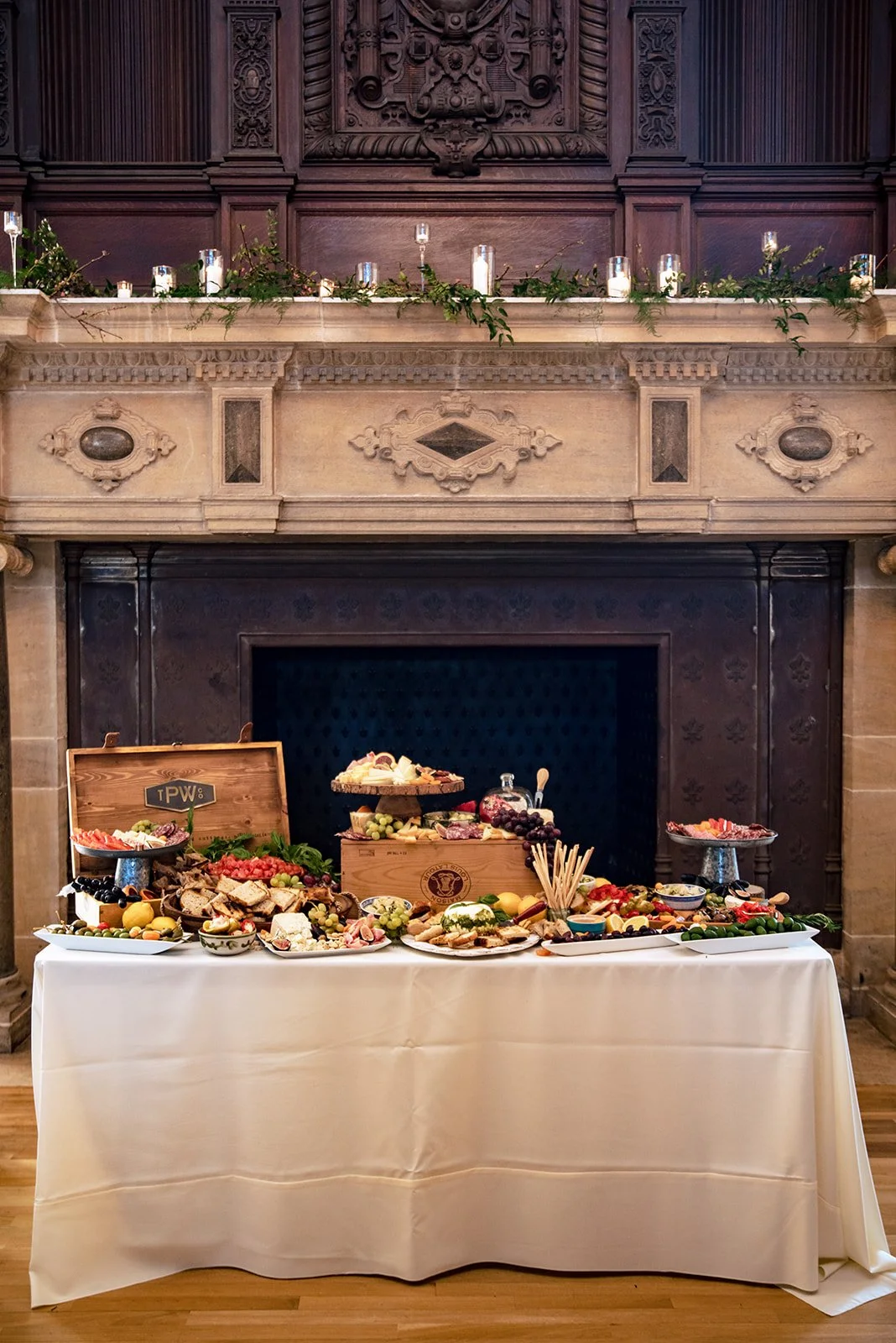 Charcuterie and cheese grazing table beneath a candlelit greenery mantel at a Branford House wedding in Groton, CT