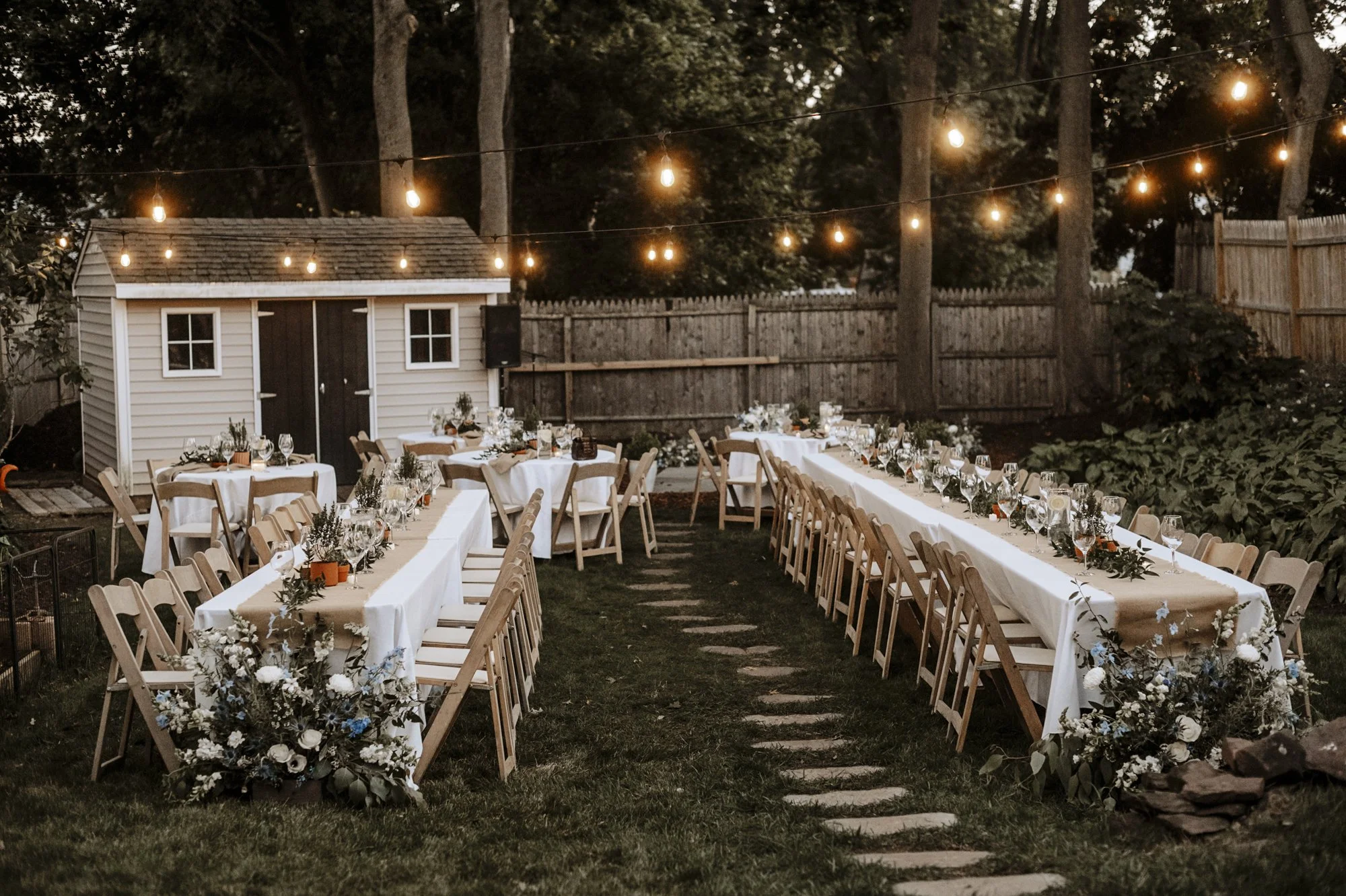 Backyard wedding reception tables with Italian ruscus greenery laid along long tables and gathered on rounds, in Hamden, Connecticut