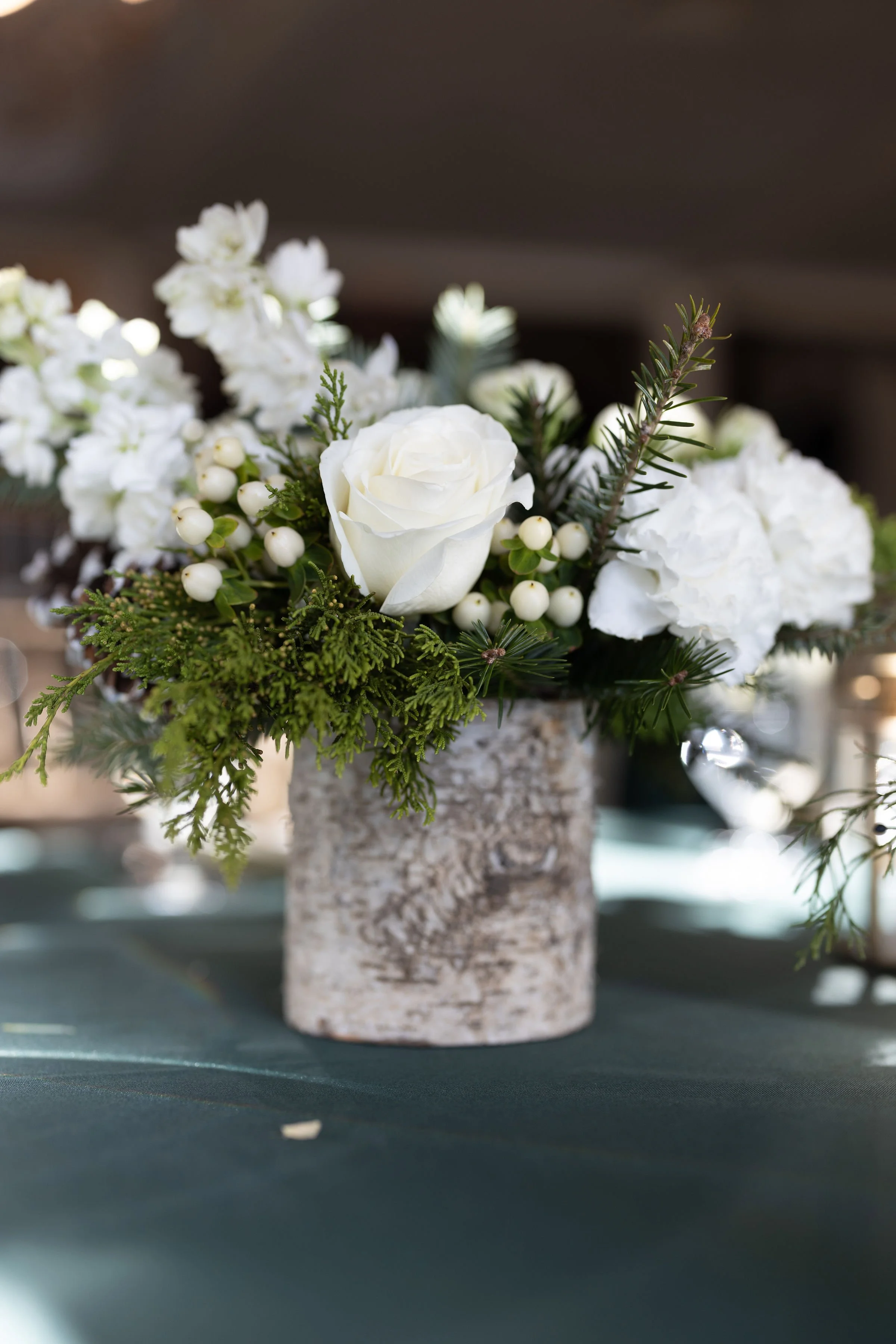 Winter white centerpiece of white roses, hypericum berries and evergreen foliage in a birch bark pot at The Inn at Longshore in Westport, Connecticut