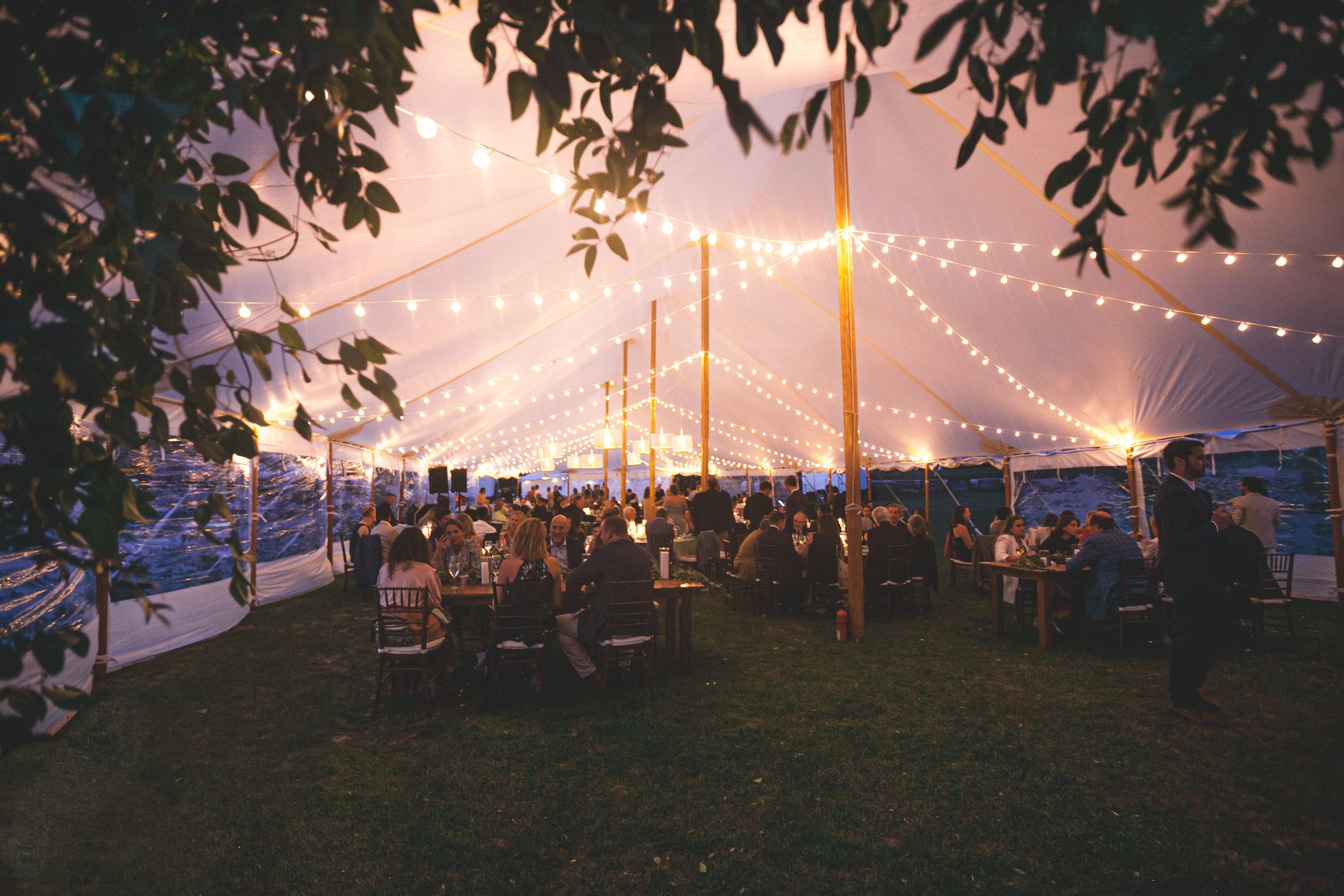 A greenery-wrapped arch marks the entrance to the reception tent, with guests gathered just beyond at a Saybrook Point wedding.
