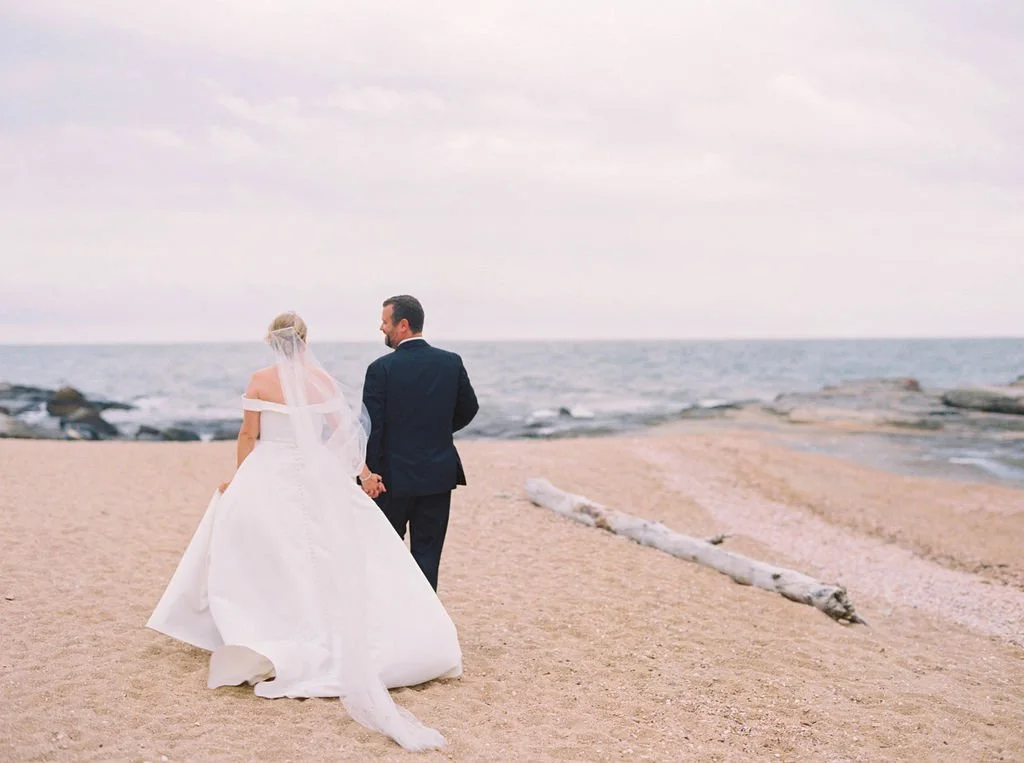 Connecticut coastal bride in off-the-shoulder ivory gown with flowing veil caught in the wind.