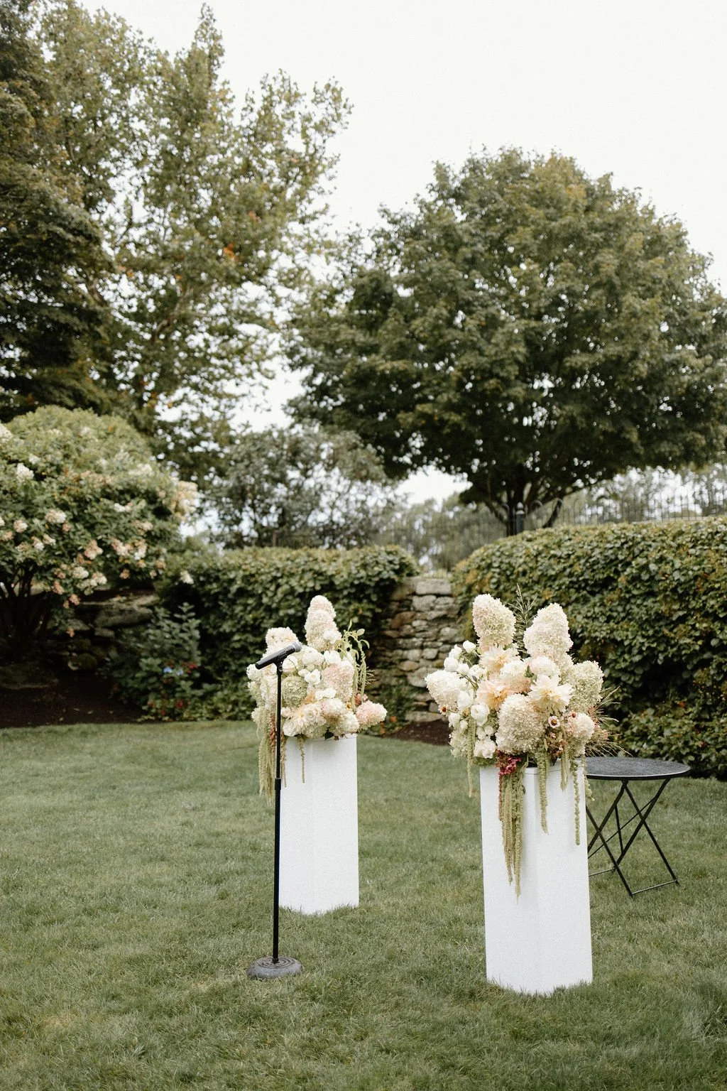 Two white ceremony columns topped with airy neutral floral arrangements in the gardens.