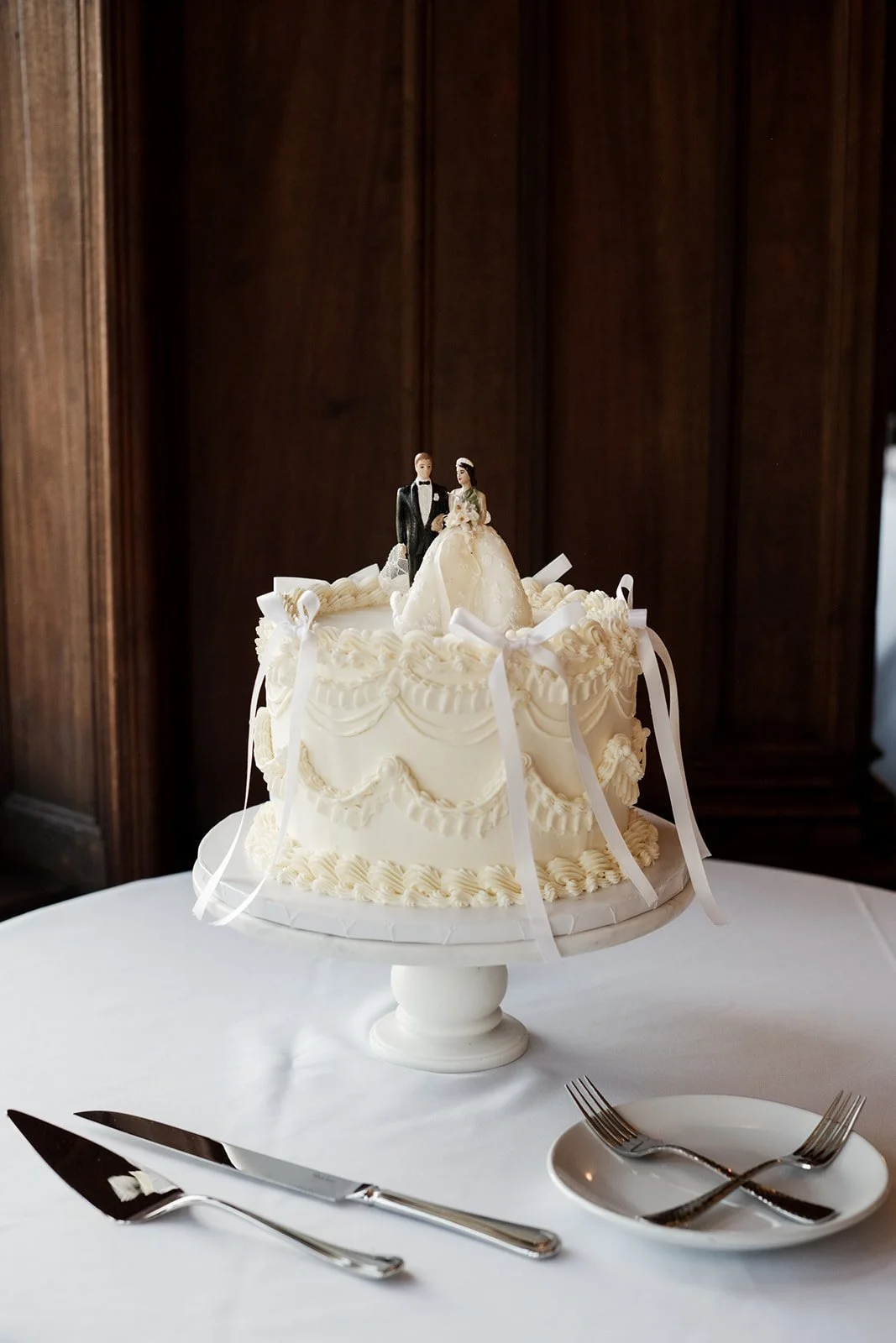 All-white Lambeth cake with delicate ribbon details and a vintage wedding cake topper.