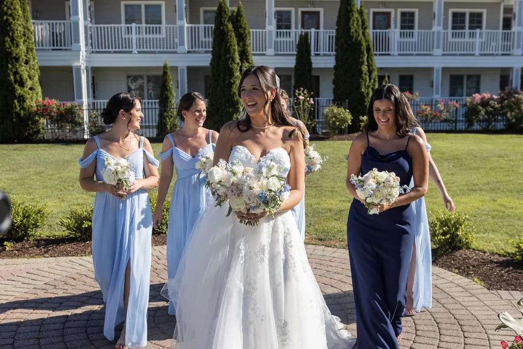 Bride and bridesmaids in light blue and navy gowns walking with white and blue wedding bouquets at Water's Edge Resort and Spa Connecticut, garden style wedding flowers by First Blush Floral Design