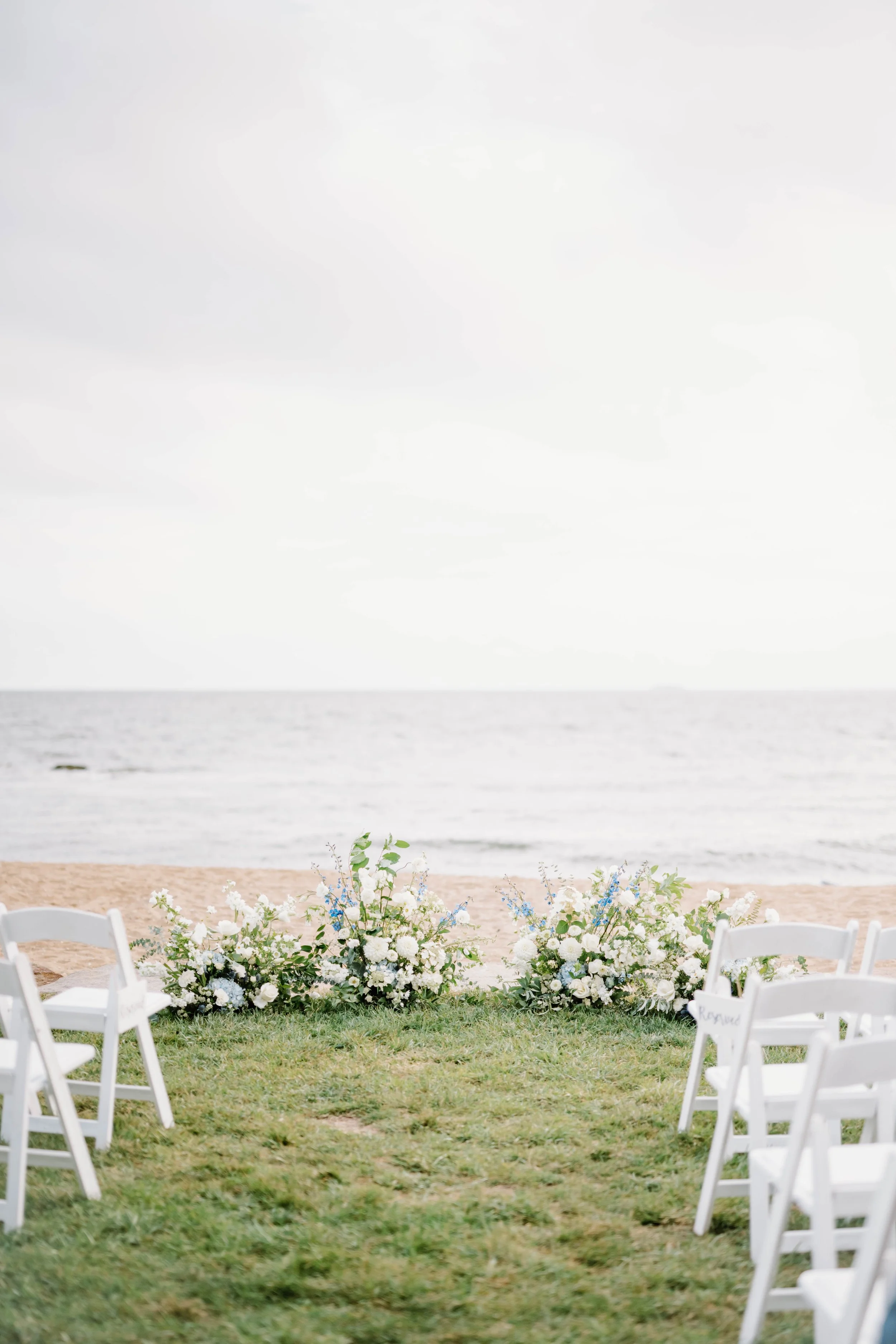 Grounded floral meadow of white hydrangea, blue thistle, and sage foliage framing ceremony on waterfront lawn.