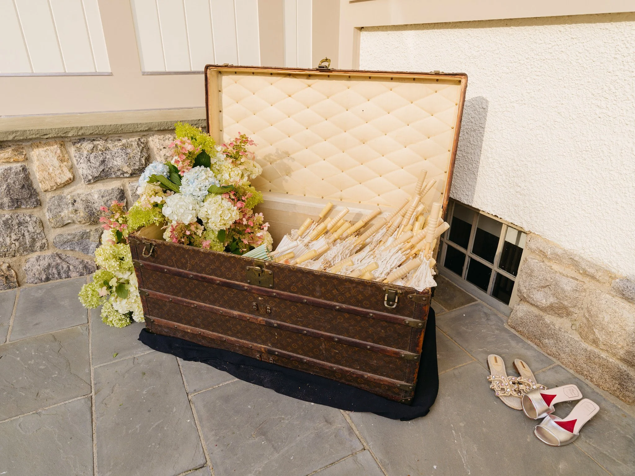 Vintage Louis Vuitton trunk repurposed to hold lace parasols and hydrangea blooms, coastal bridal shower styling