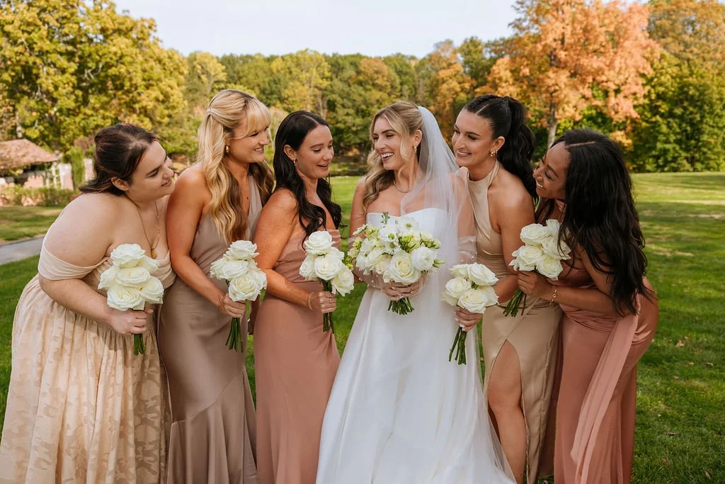 Bride with long wavy blonde hair laughing with bridesmaids in neutral dresses at Waveny House
