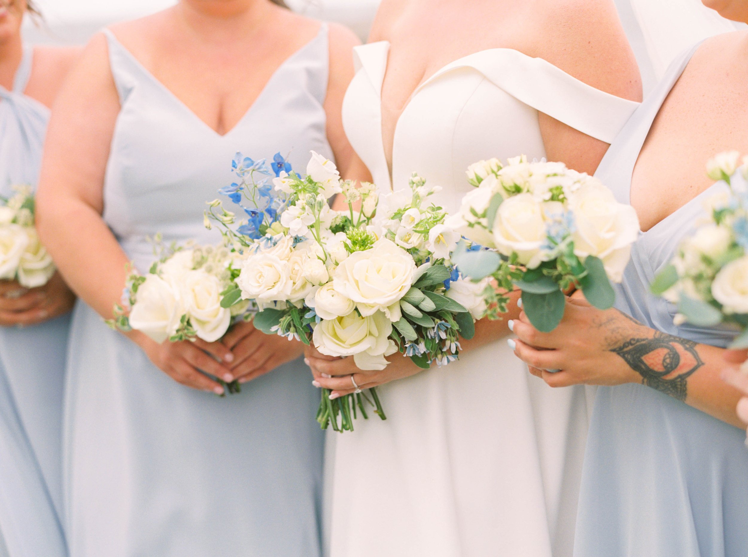 Bridesmaids in dusty-blue gowns carrying smaller posy bouquets of white and blue flowers.