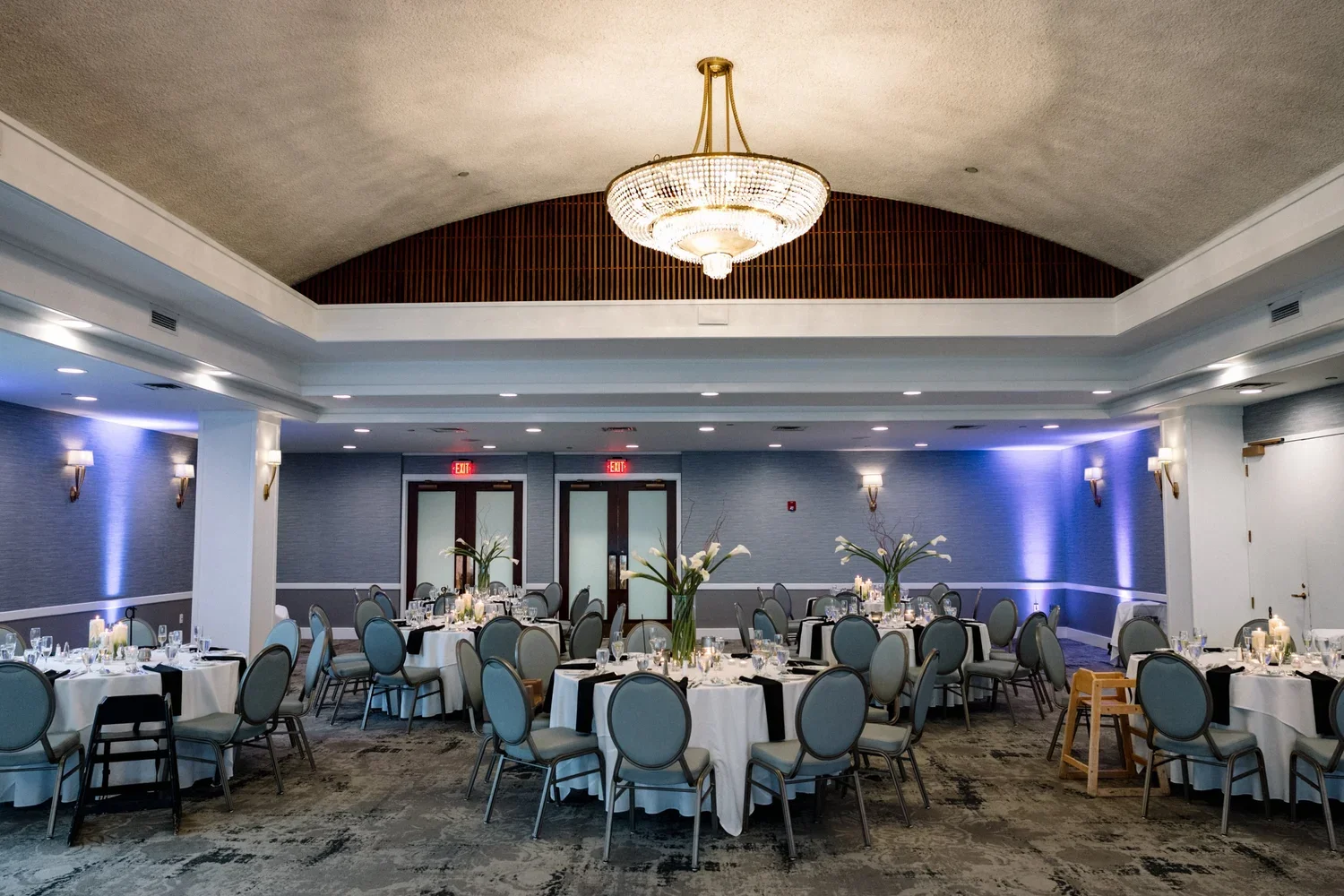 Waters Edge reception flowers by First Blush Weddings featuring long white calla lilies and reaching branches in elevated glass cylinders alternating with cut calla flowers.