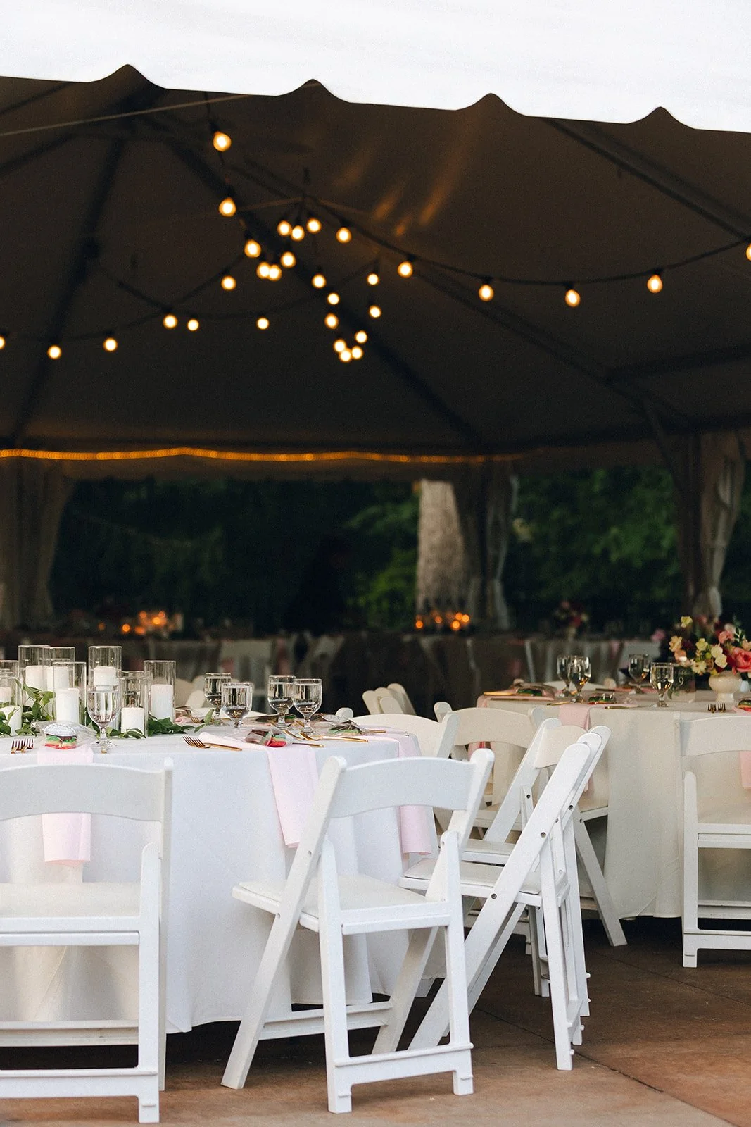 Tented wedding reception at Wickham Park with white chairs, elegantly styled tables, floral centerpieces and warm overhead string lights.
