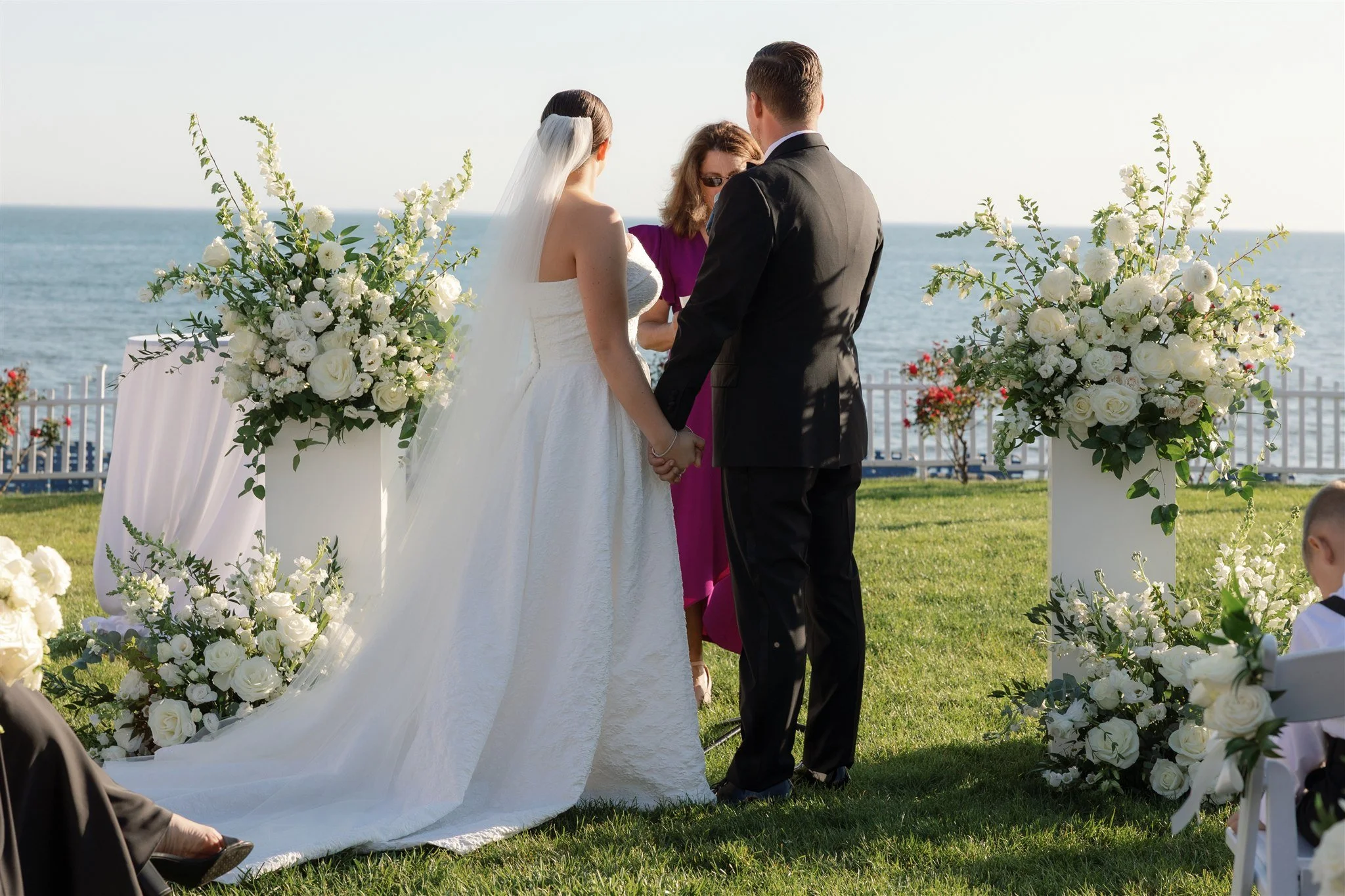 Couple standing between sculptural white floral columns during their outdoor ceremony at Water’s Edge.