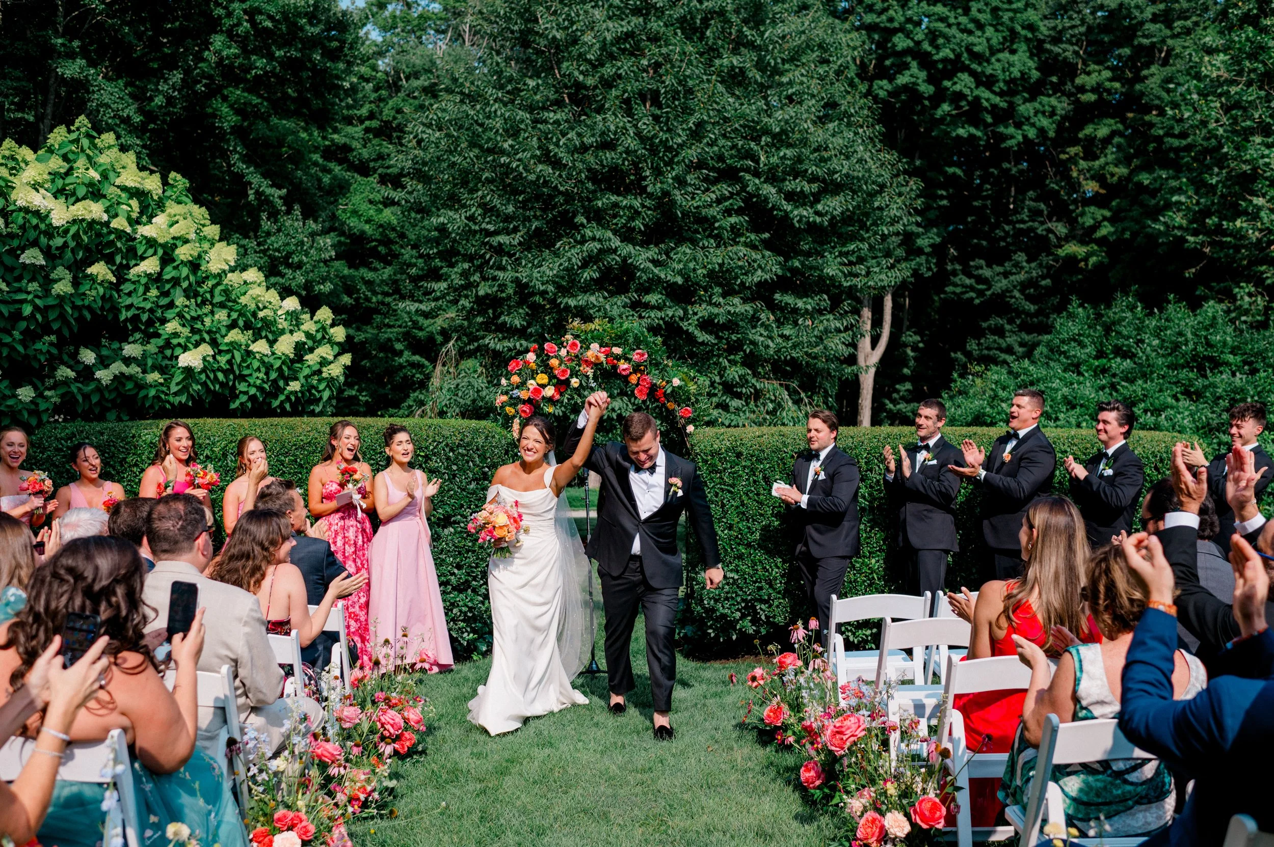 Garden ceremony setup with white chairs and cheerful ombré floral aisle design.