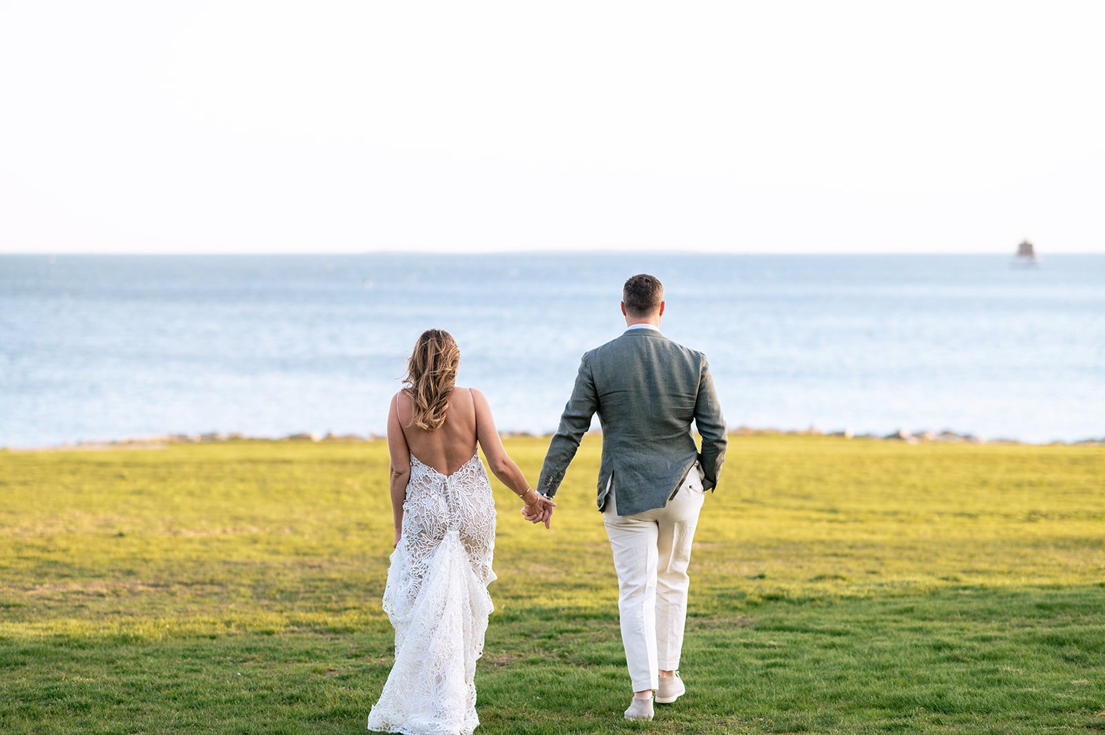 Groom in a light grey blazer and white trousers beside his bride at golden hour on the Connecticut shoreline