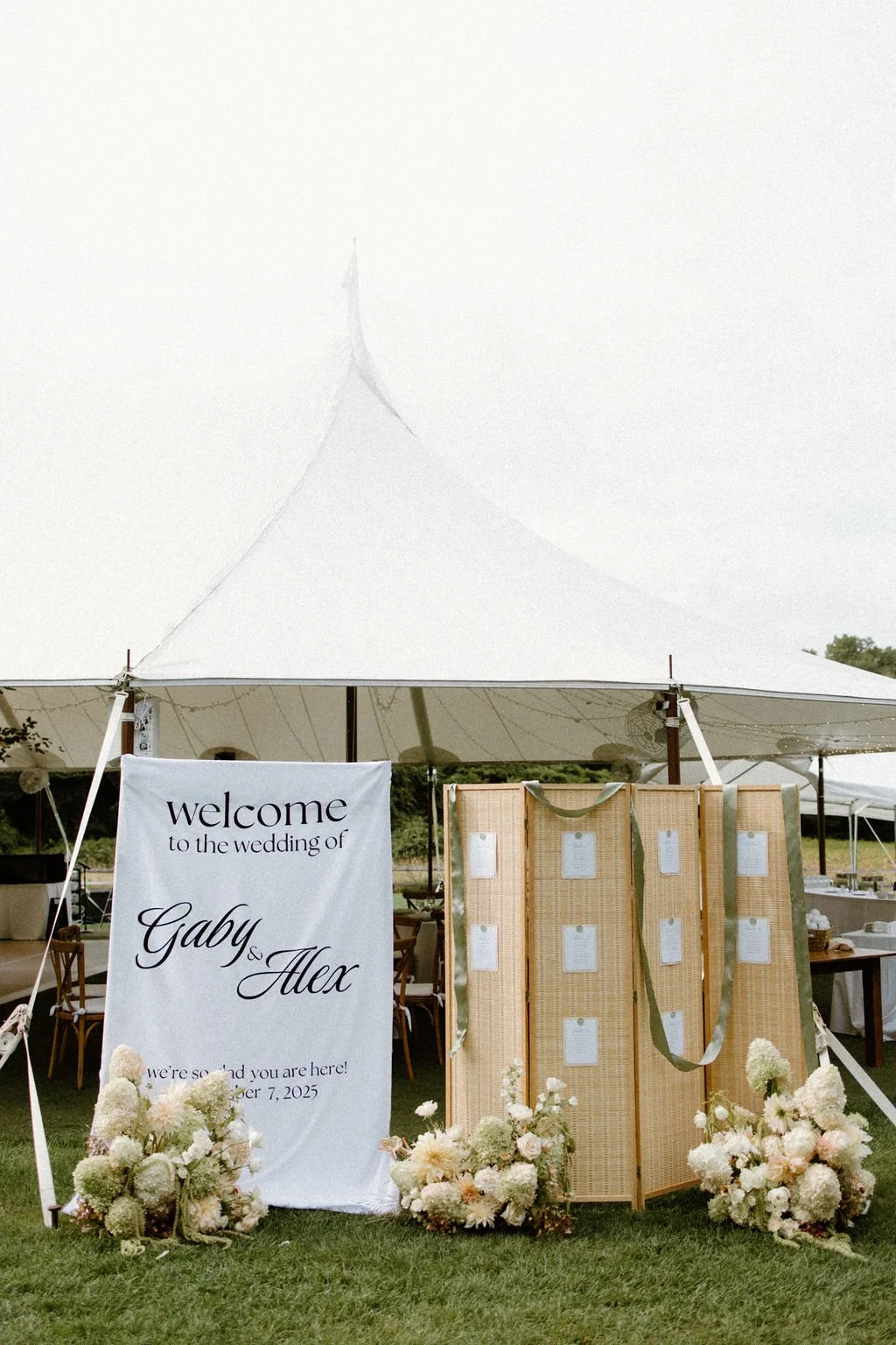 Wedding welcome signage and garden floral details beside the outdoor reception tent.
